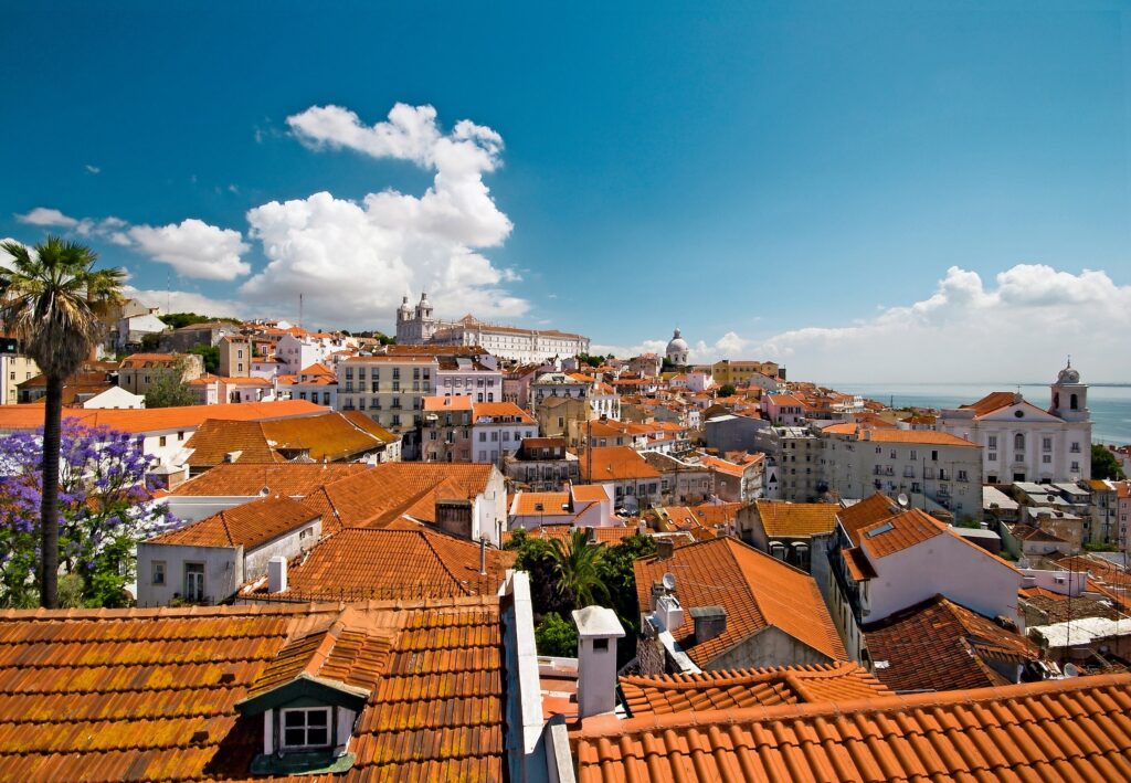 Stadtansicht von Lissabon mit roten Dächern und blauen Himmel, umgeben von historischen Gebäuden.