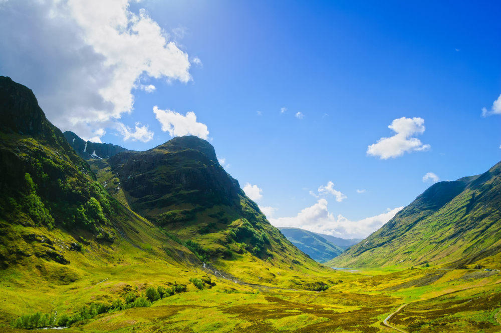 Grüne Berglandschaft mit blauen Himmel und Wolken im Glen Coe, Schottland.