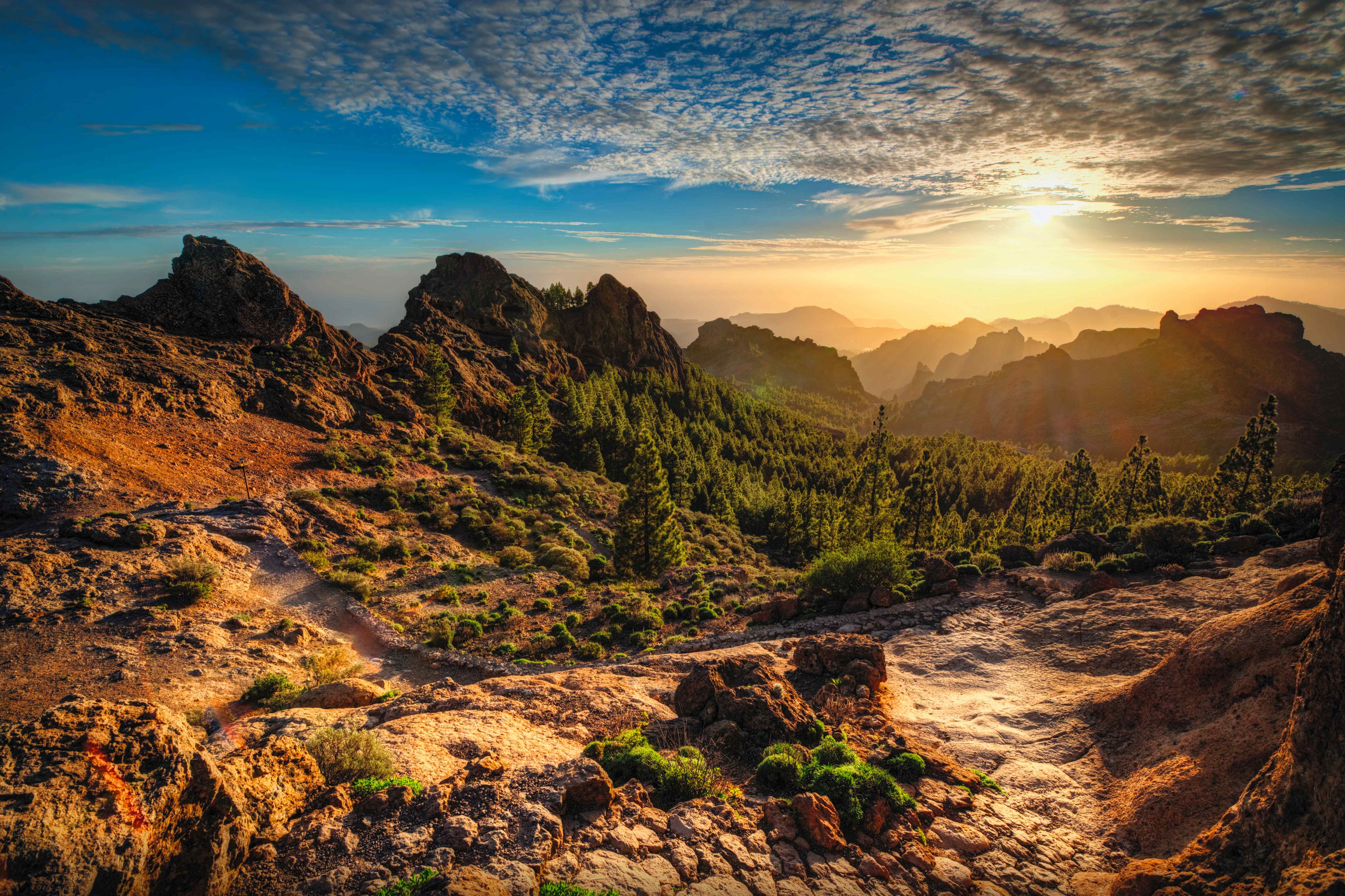 Berglandschaft auf Gran Canaria mit Sonnenuntergang und bewaldeten Hügeln im Hintergrund.