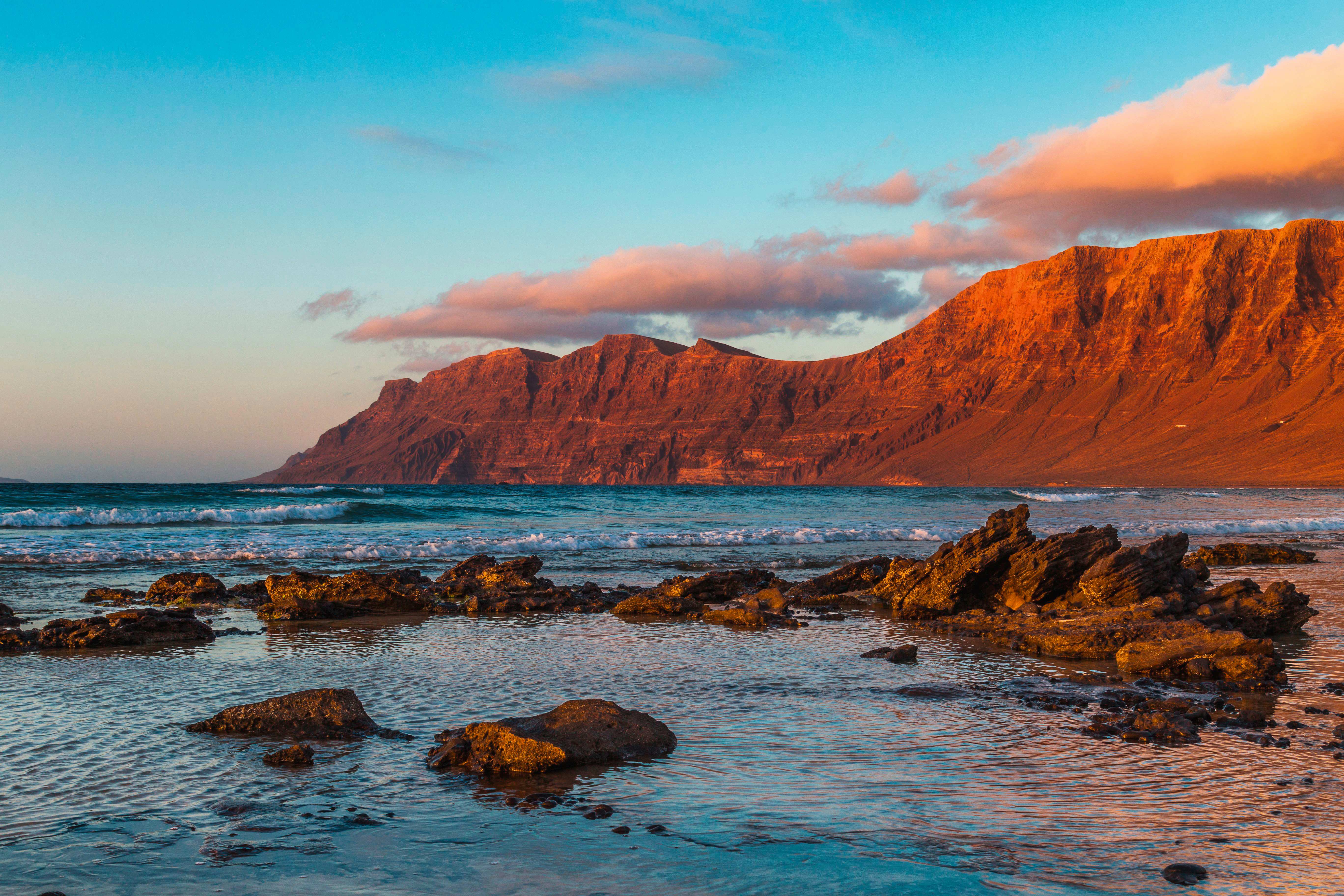 Famaraklippen auf Lanzarote mit Wasser und Felsen im Vordergrund bei Sonnenuntergang.