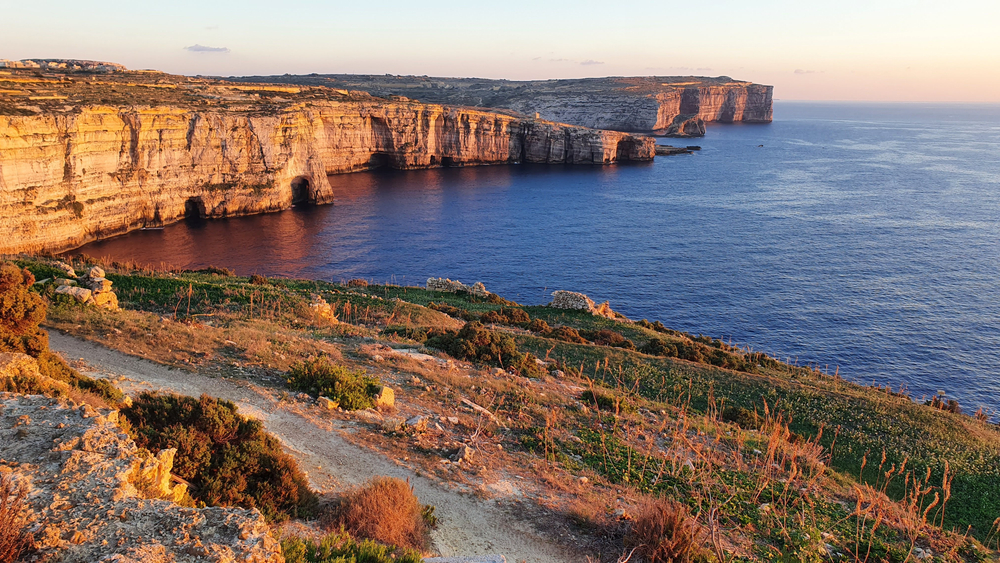Küstenlandschaft von Gozo mit Klippen und ruhigem Wasser bei Sonnenuntergang.