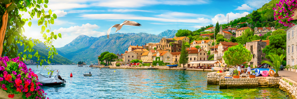 Blick auf die malerische Küstenstadt Perast in der Bucht von Kotor mit bunten Häusern und Bergen im Hintergrund.