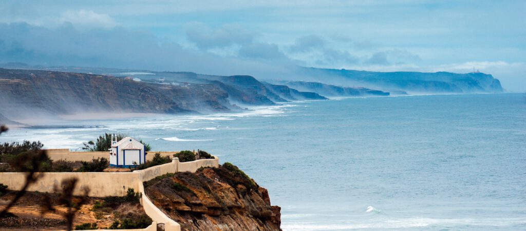 Küstenlinie von Ericeira mit sanften Wellen und bewölktem Himmel über dem Ozean.