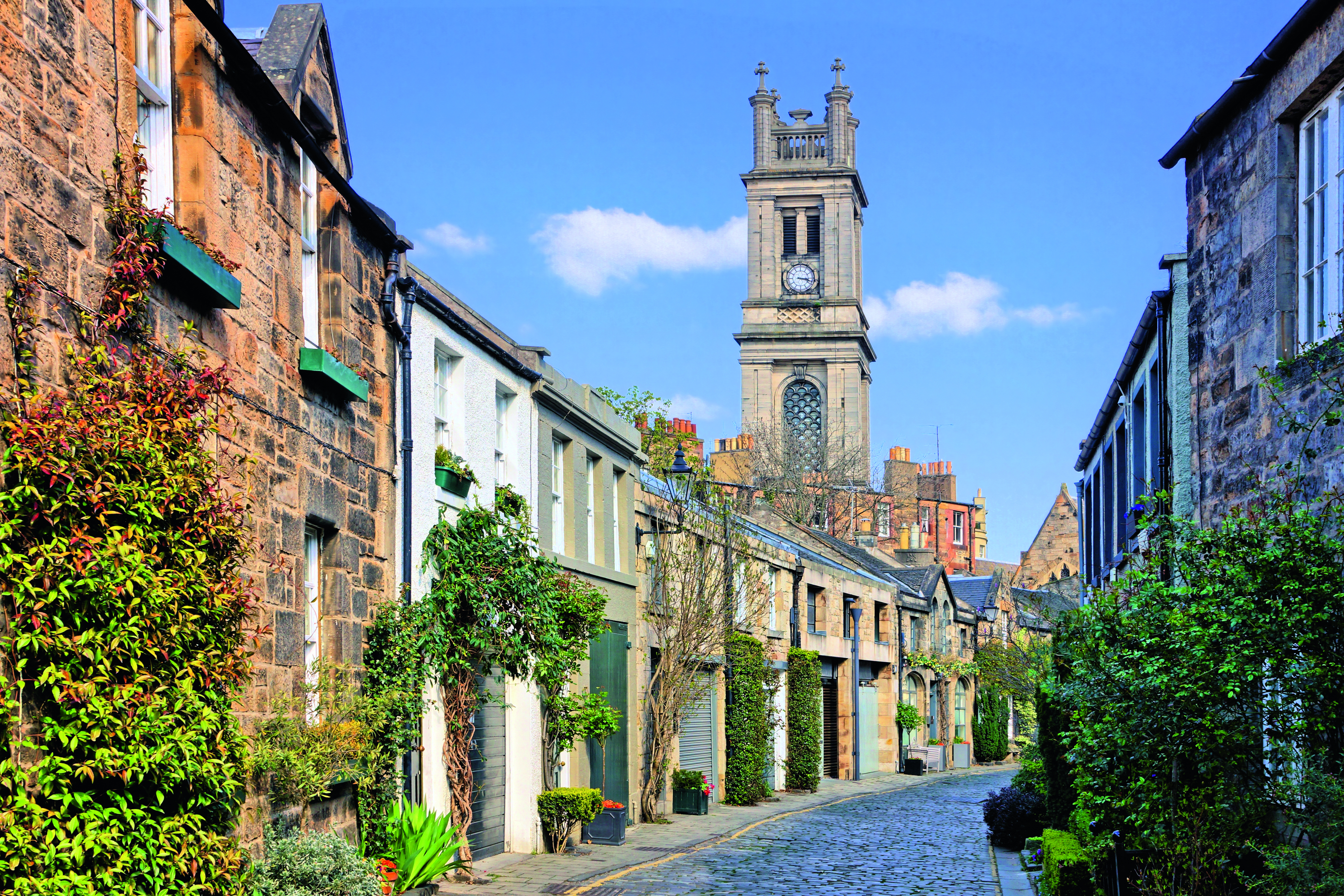 Straße in Edinburgh mit historischen Gebäuden und einem Uhrturm im Hintergrund.