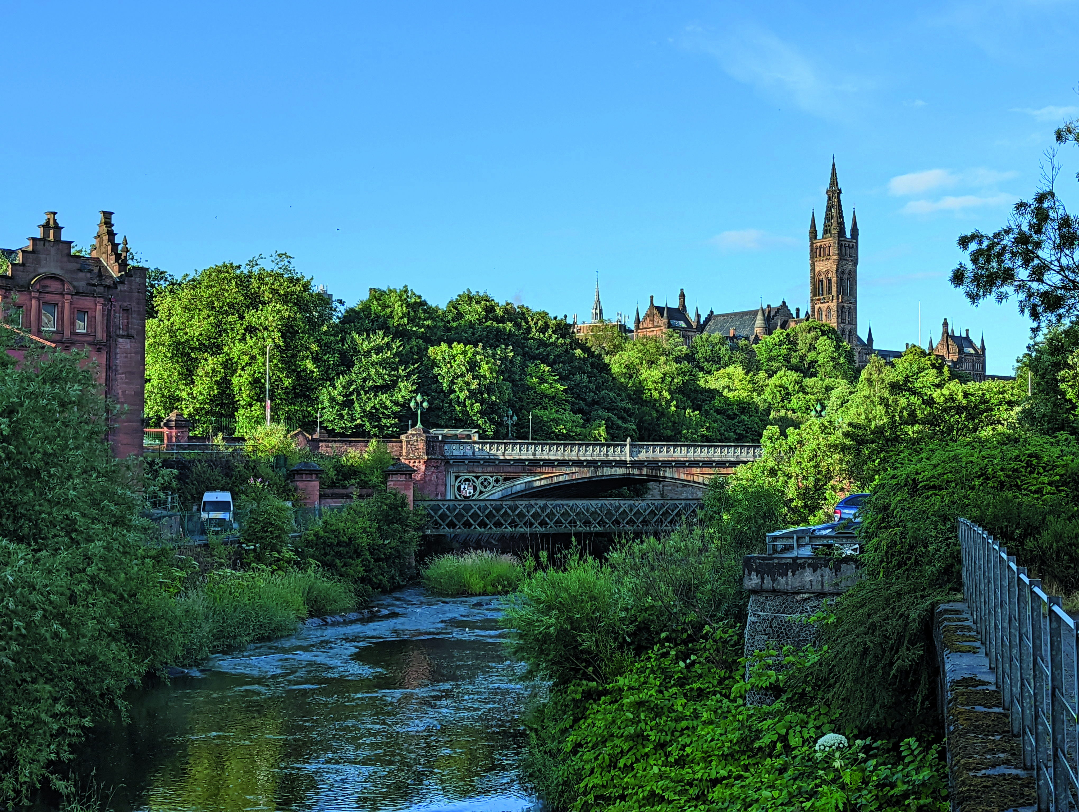 Blick auf die Glasgow University mit grüner Vegetation und einem Fluss im Vordergrund.