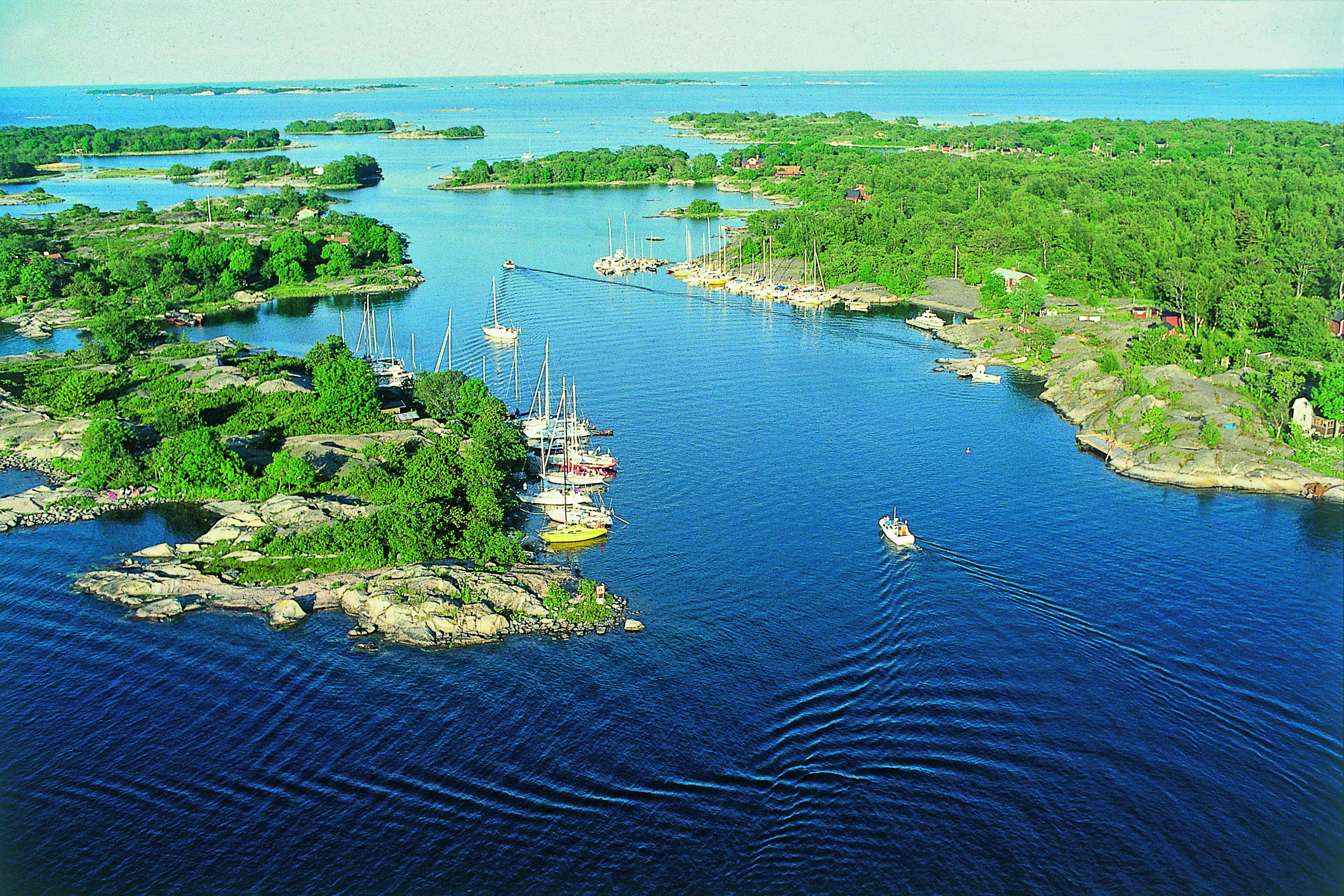 Landschaft mit Wasserwegen und Booten in einem schwedischen Archipel, umgeben von grüner Vegetation.
