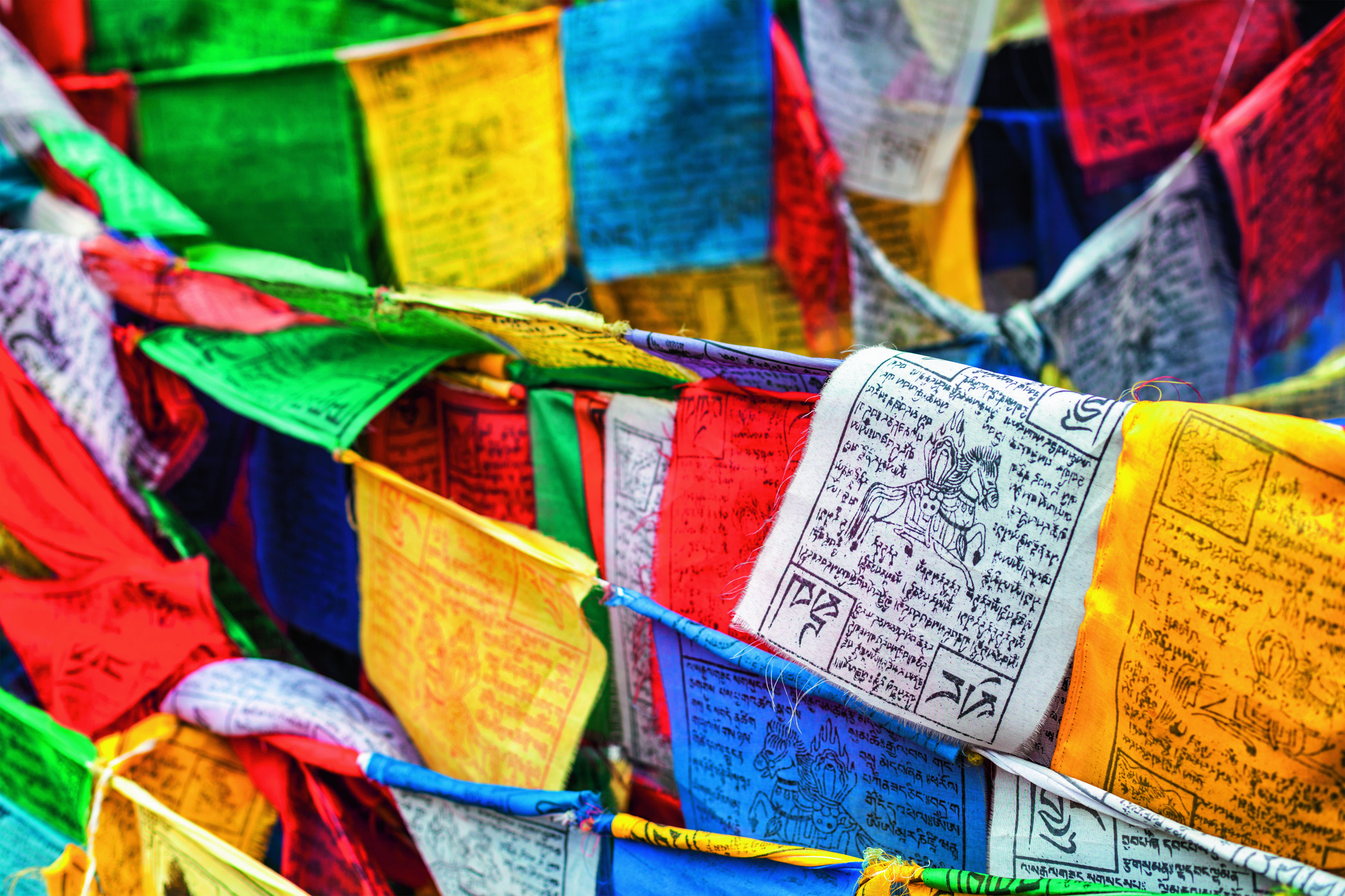 Bunte Gebetsfahnen in verschiedenen Farben wie Rot, Blau, Gelb, Grün und Weiß mit tibetischen Schriftzeichen.