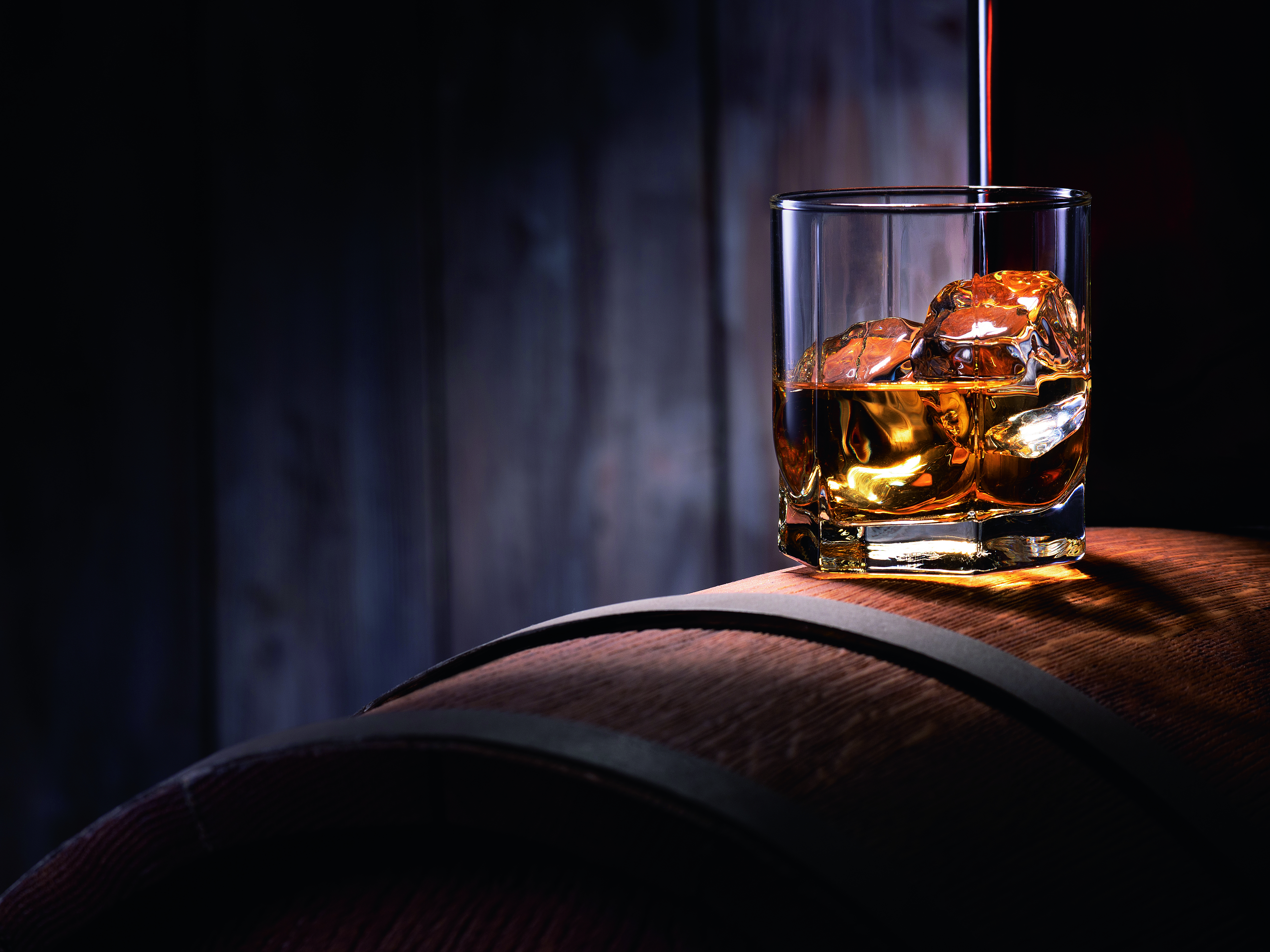Ein Glas mit irischem Whiskey, gefüllt mit Eiswürfeln, auf einem Holzfass. Der Whiskey wird in das Glas gegossen.