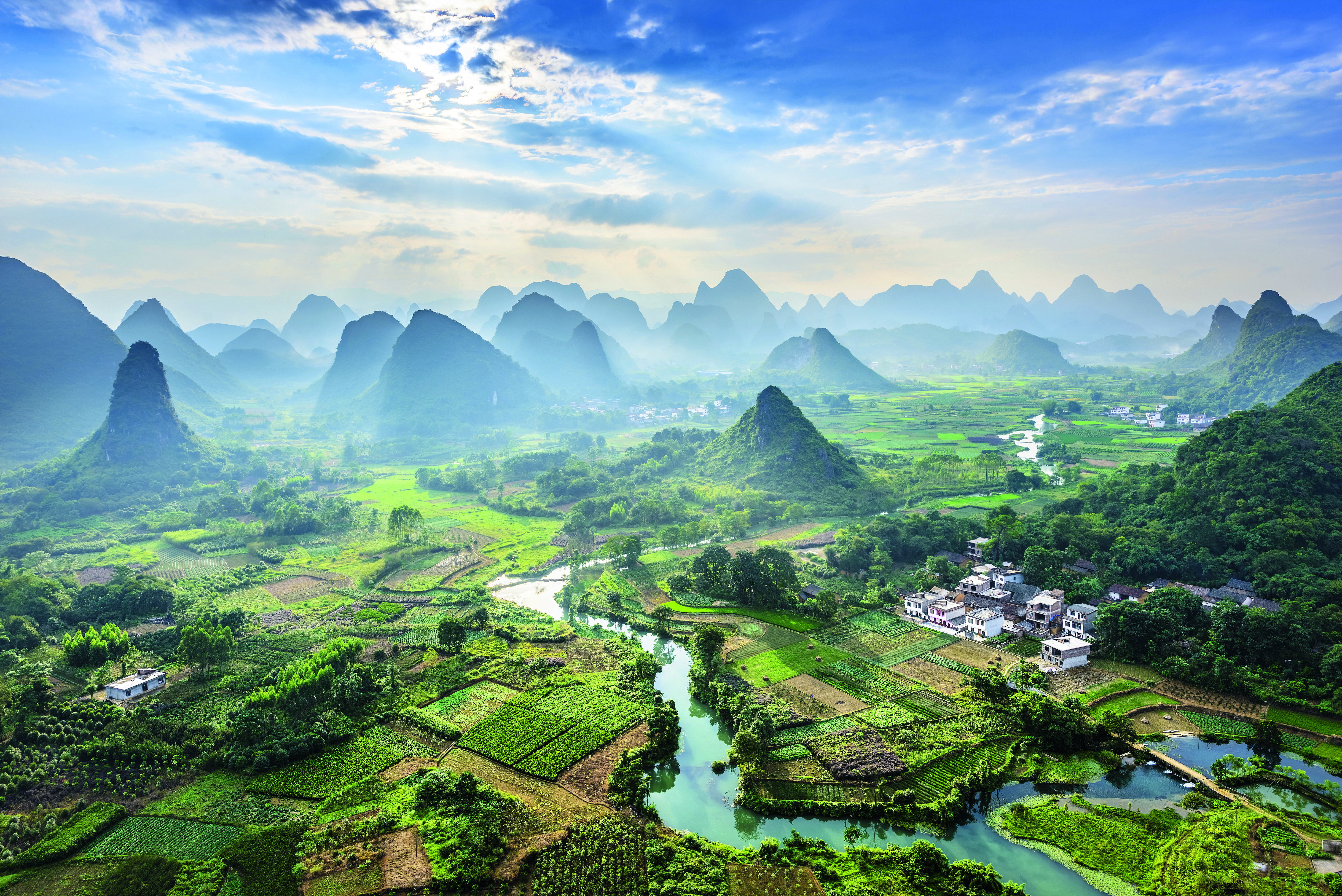 Landschaft mit grünen Feldern, Bergen und einem Fluss, der durch die Landschaft fließt.