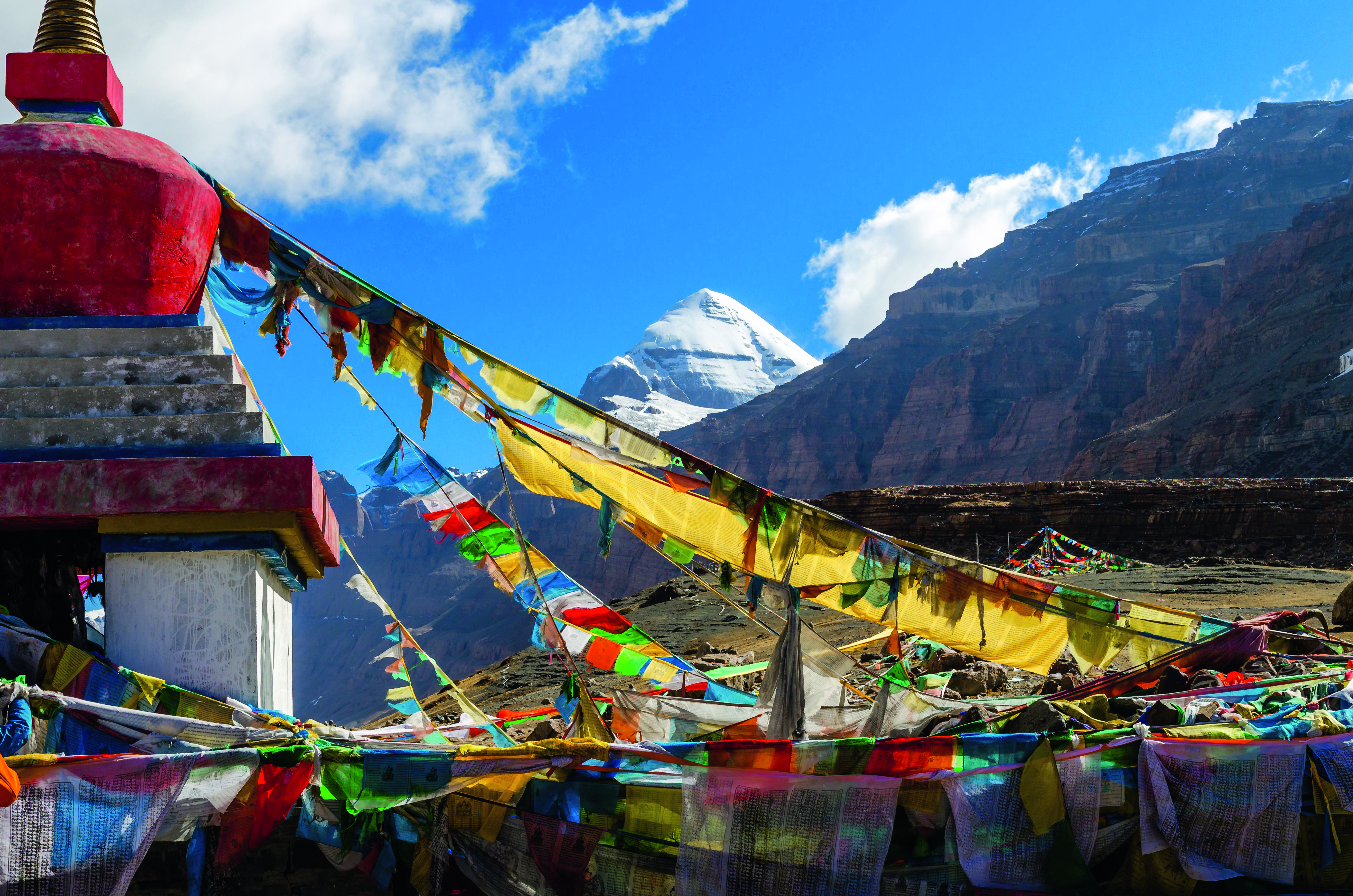 Bunte Gebetsfahnen, die am Berg Kailash wehen, mit schneebedecktem Gipfel im Hintergrund.