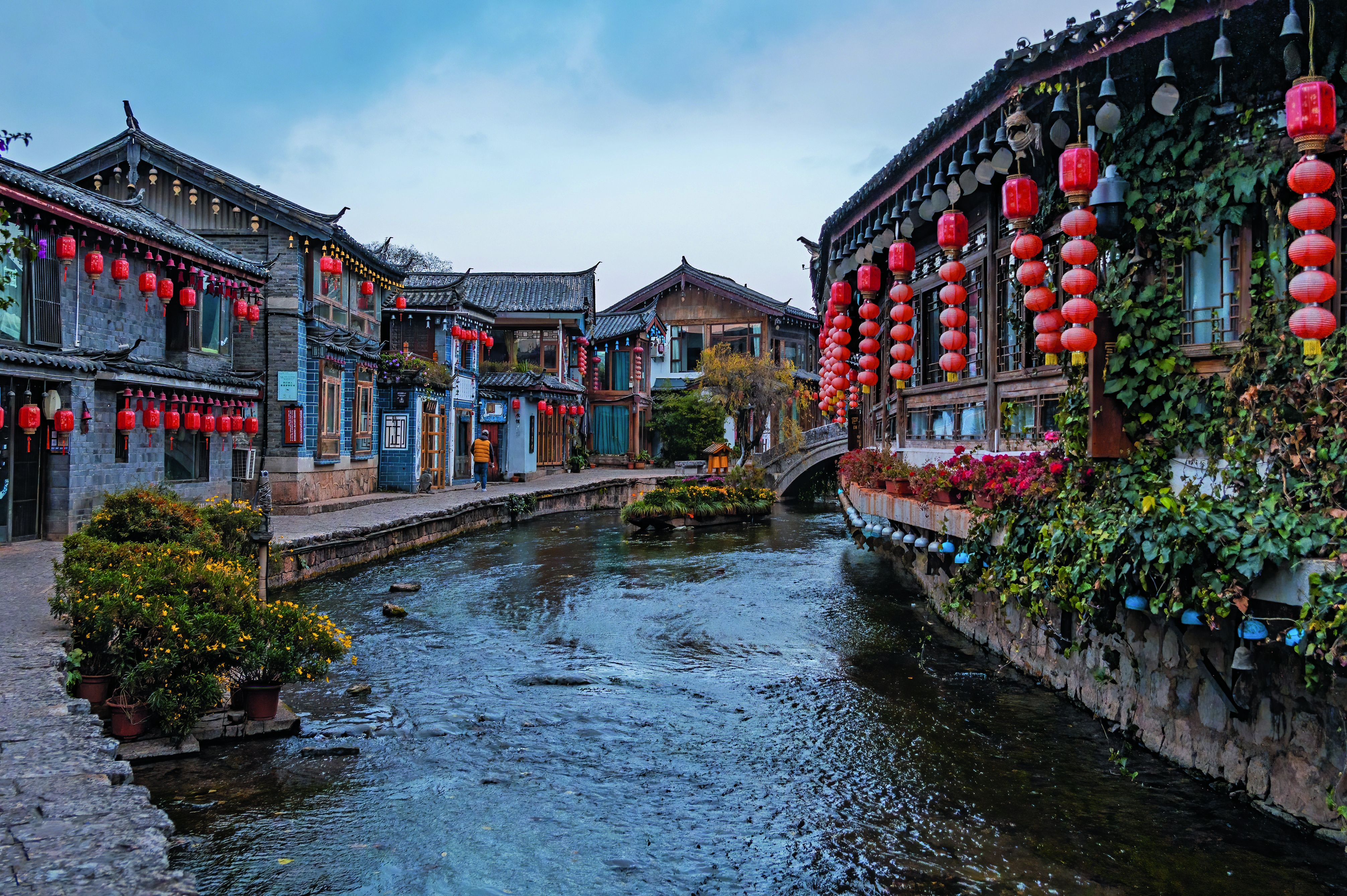 Altstadt von Lijiang mit roten Laternen und einem ruhigen Kanal, umgeben von traditionellen Gebäuden.