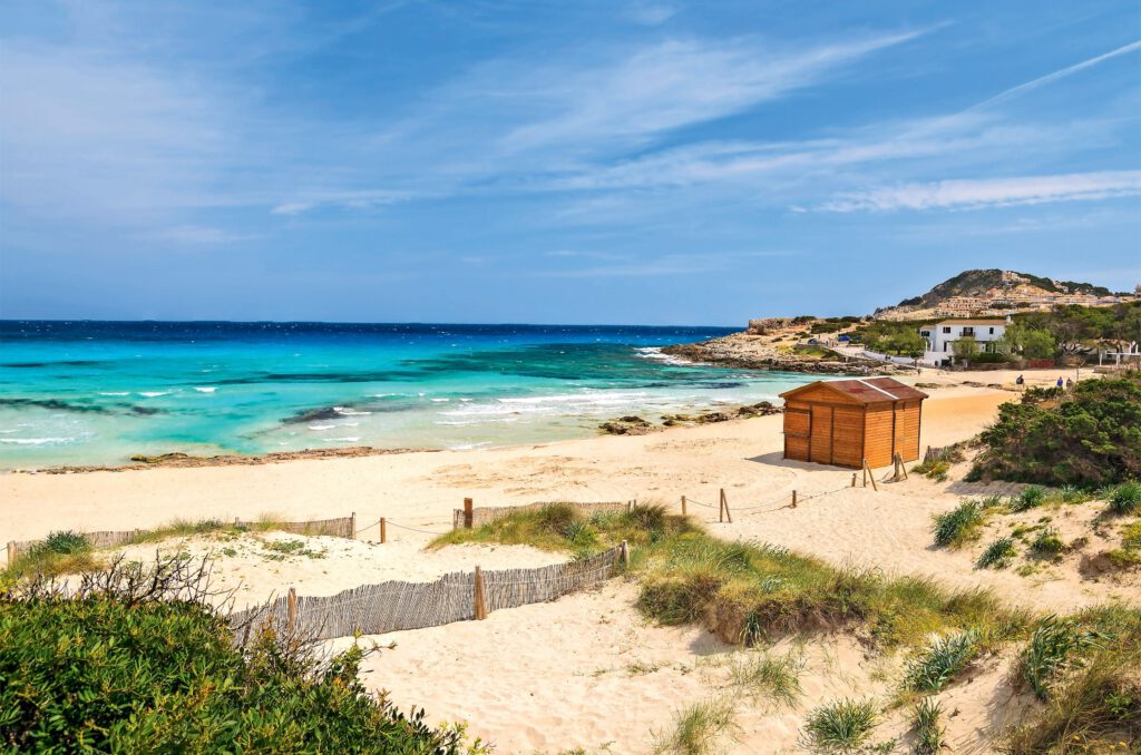 Strandlandschaft mit einem Holzhaus und klarem Wasser in Cala Agulla, Mallorca.