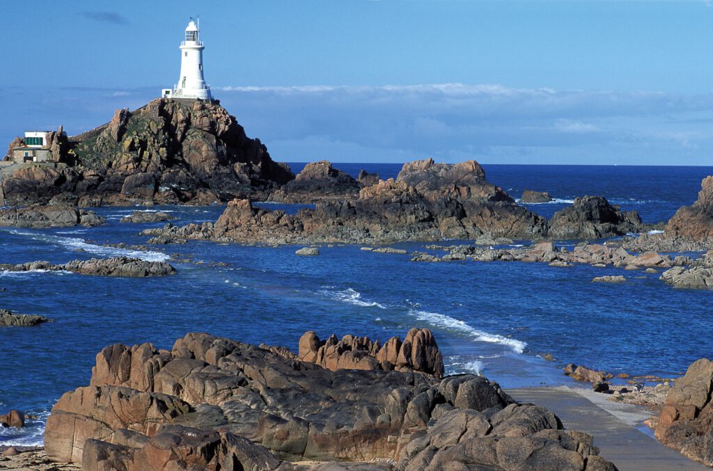 Leuchtturm auf einer felsigen Küste mit klarem blauen Wasser im Hintergrund.