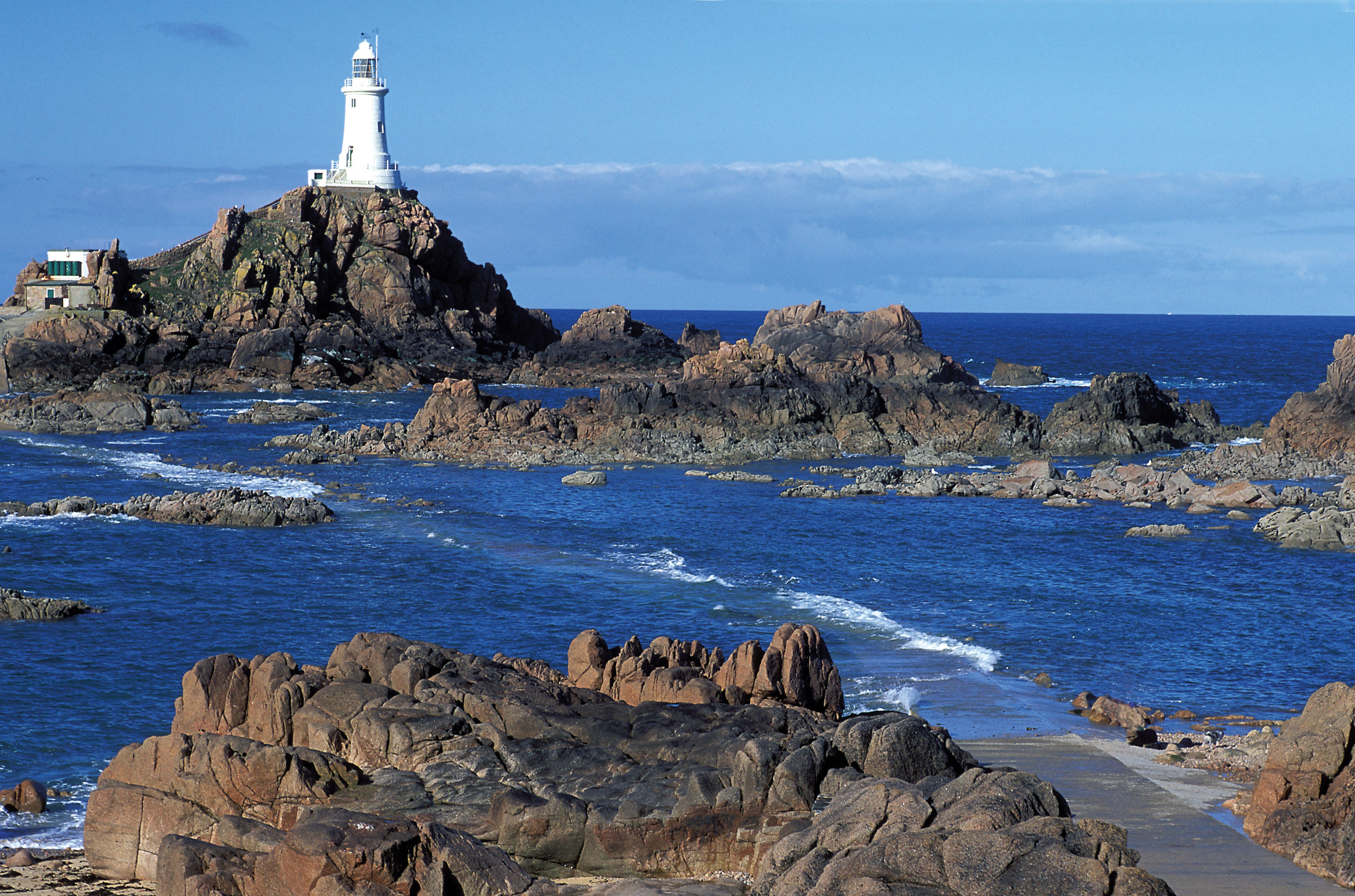 Leuchtturm auf einer felsigen Küste mit klarem blauen Wasser im Hintergrund.