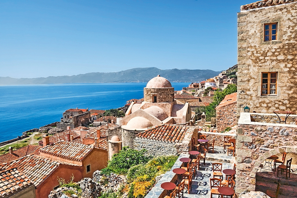 Blick auf die Küstenstadt Monemvasia mit traditionellen Gebäuden und einer Kirche mit Kuppel.