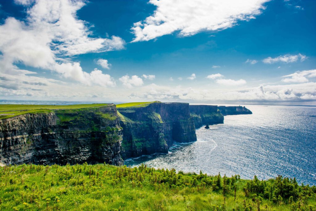 Die Cliffs of Moher in Irland mit steilen Klippen und Blick auf den Ozean unter einem blauen Himmel.