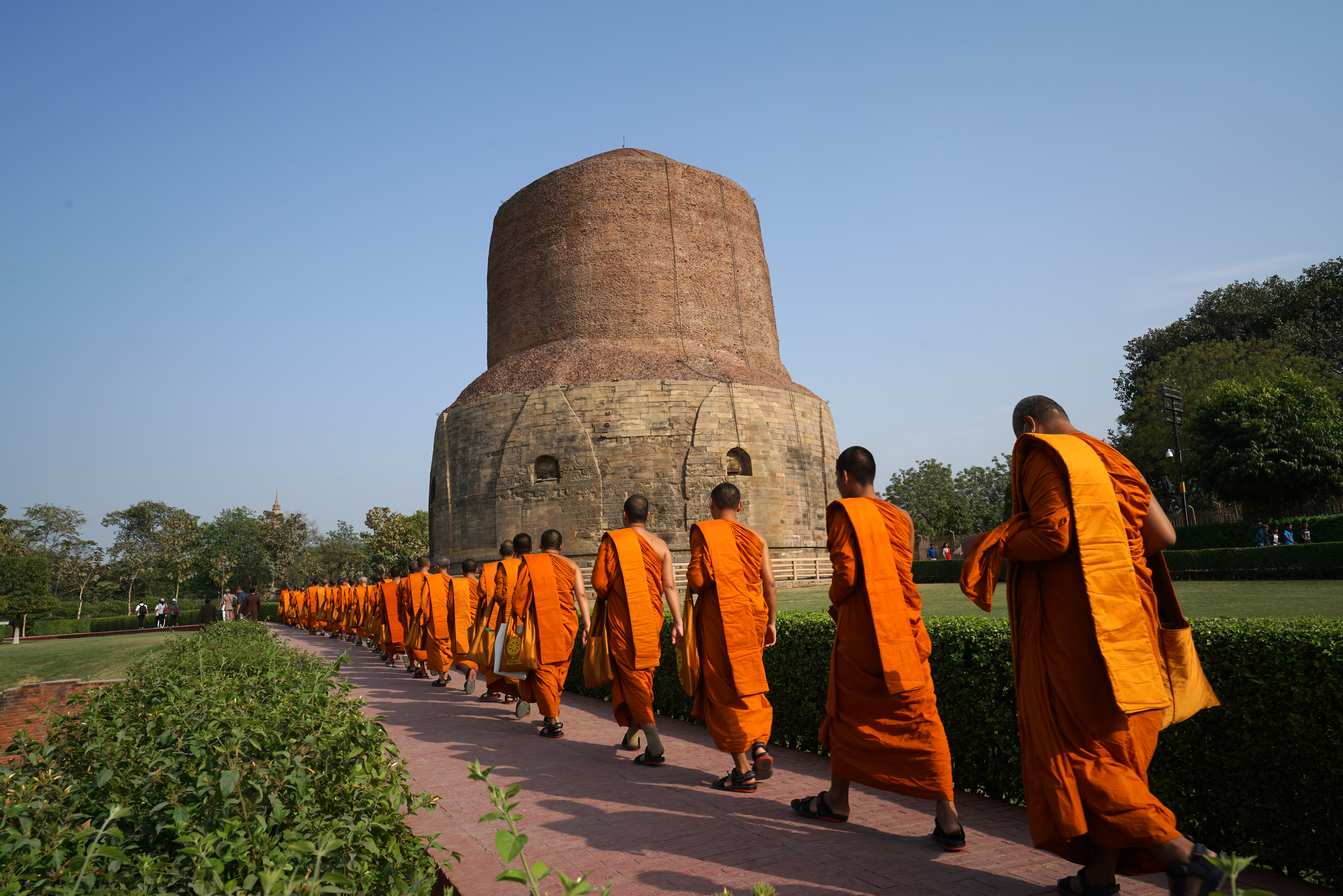 Mönche in orangefarbener Robe gehen in einer Reihe zum Dhamekh Stupa in Indien.