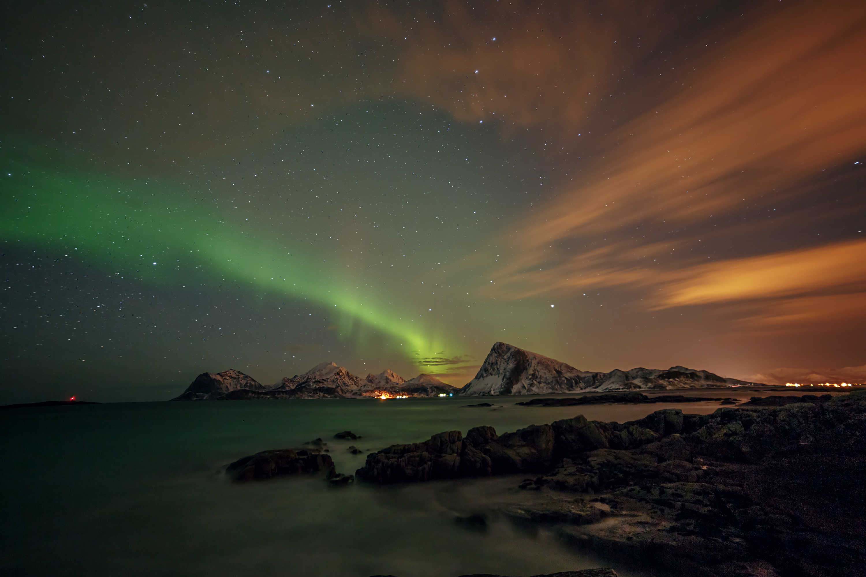 Nordlichter über einer Gebirgslandschaft mit Wasser und Wolken in der Nacht.
