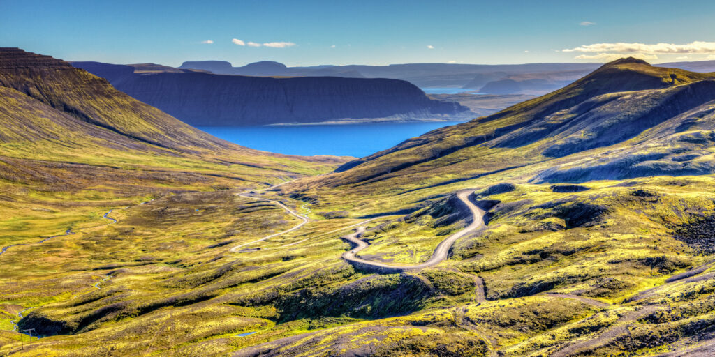 Landschaft der Westfjorde in Island mit grünen Hügeln und einem blauen See im Hintergrund.