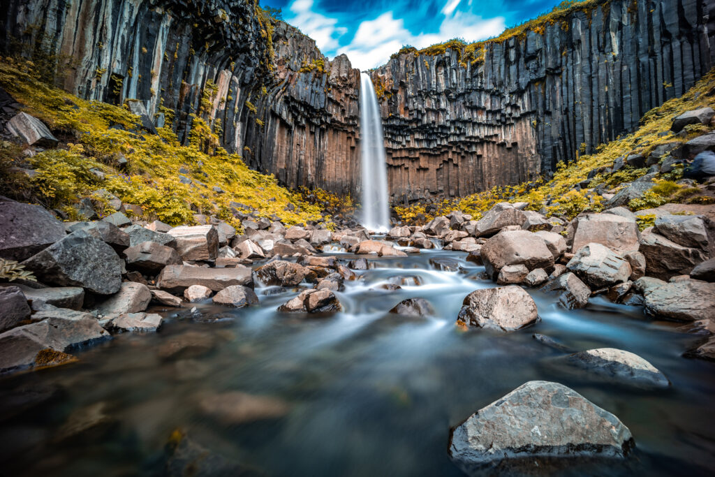 Schwarzer Wasserfall Svartifoss in Island, umgeben von basaltischen Säulen und einer klaren Wasseroberfläche.