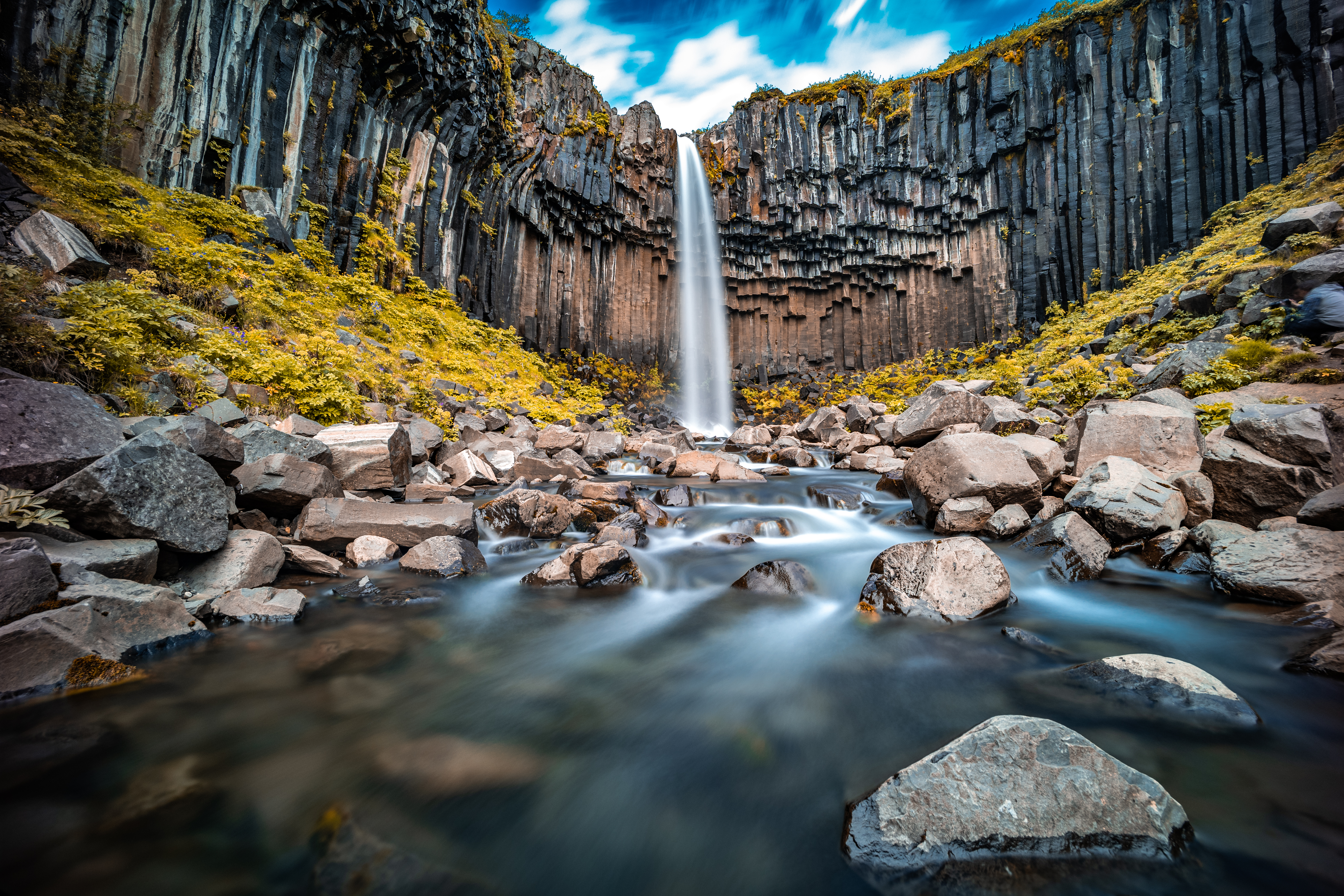 Schwarzer Wasserfall Svartifoss in Island, umgeben von basaltischen Säulen und einer klaren Wasseroberfläche.