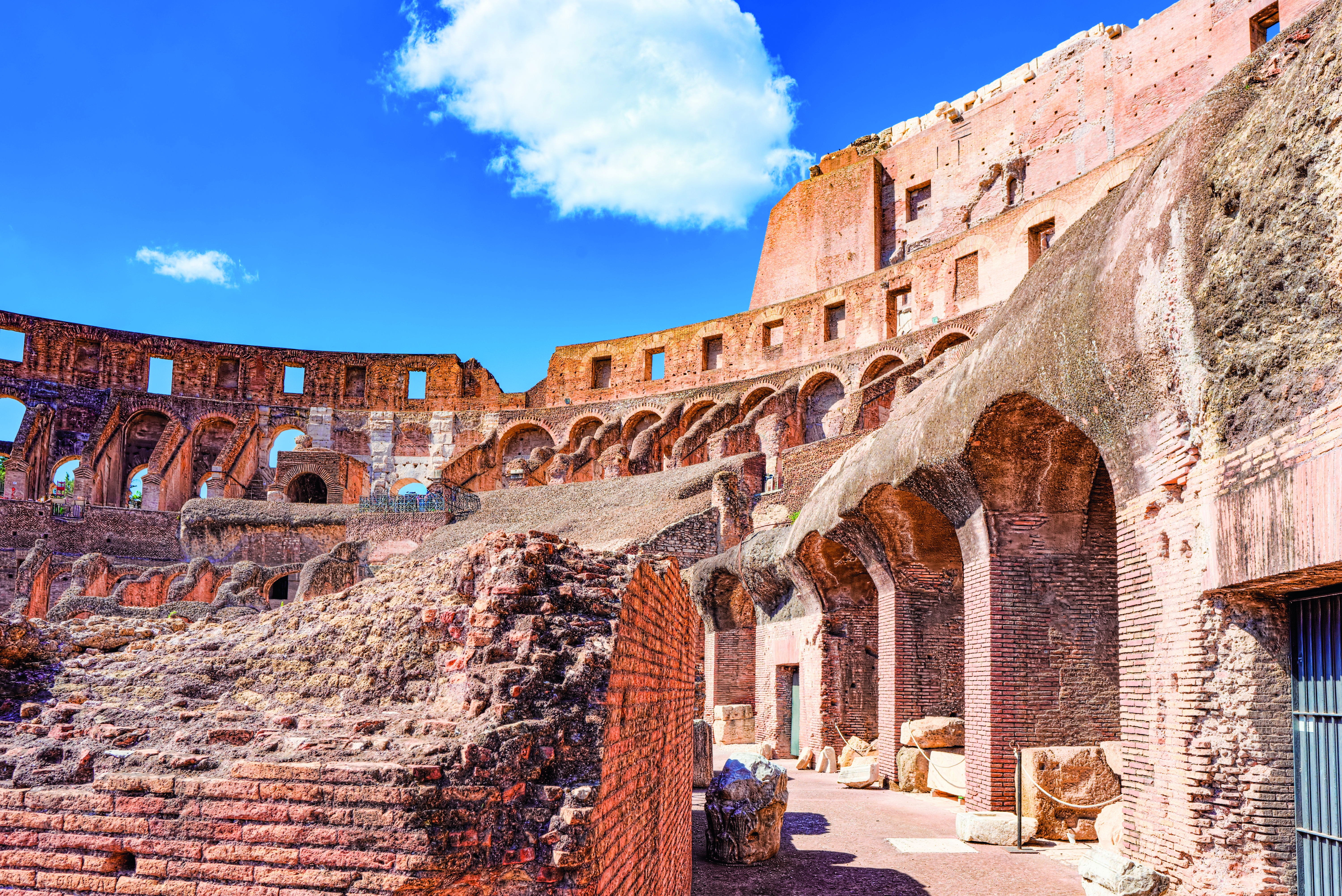 Ruinen des Kolosseums in Rom mit sichtbaren Bögen und Steinstrukturen unter blauem Himmel.