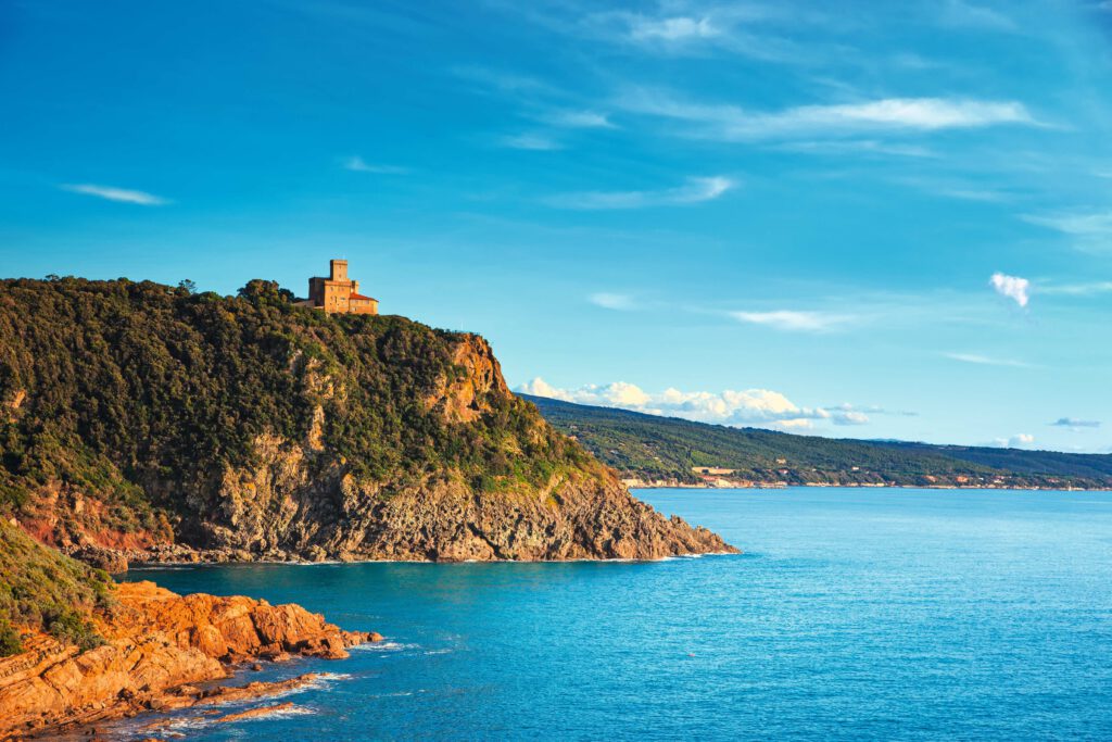 Blick auf eine Küstenlandschaft mit einem historischen Gebäude auf einem Hügel über dem blauen Wasser.