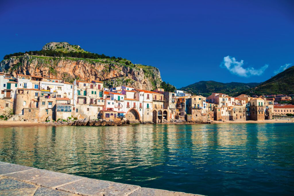 Blick auf die Küstenstadt Cefalù mit bunten Gebäuden und einem Berg im Hintergrund.