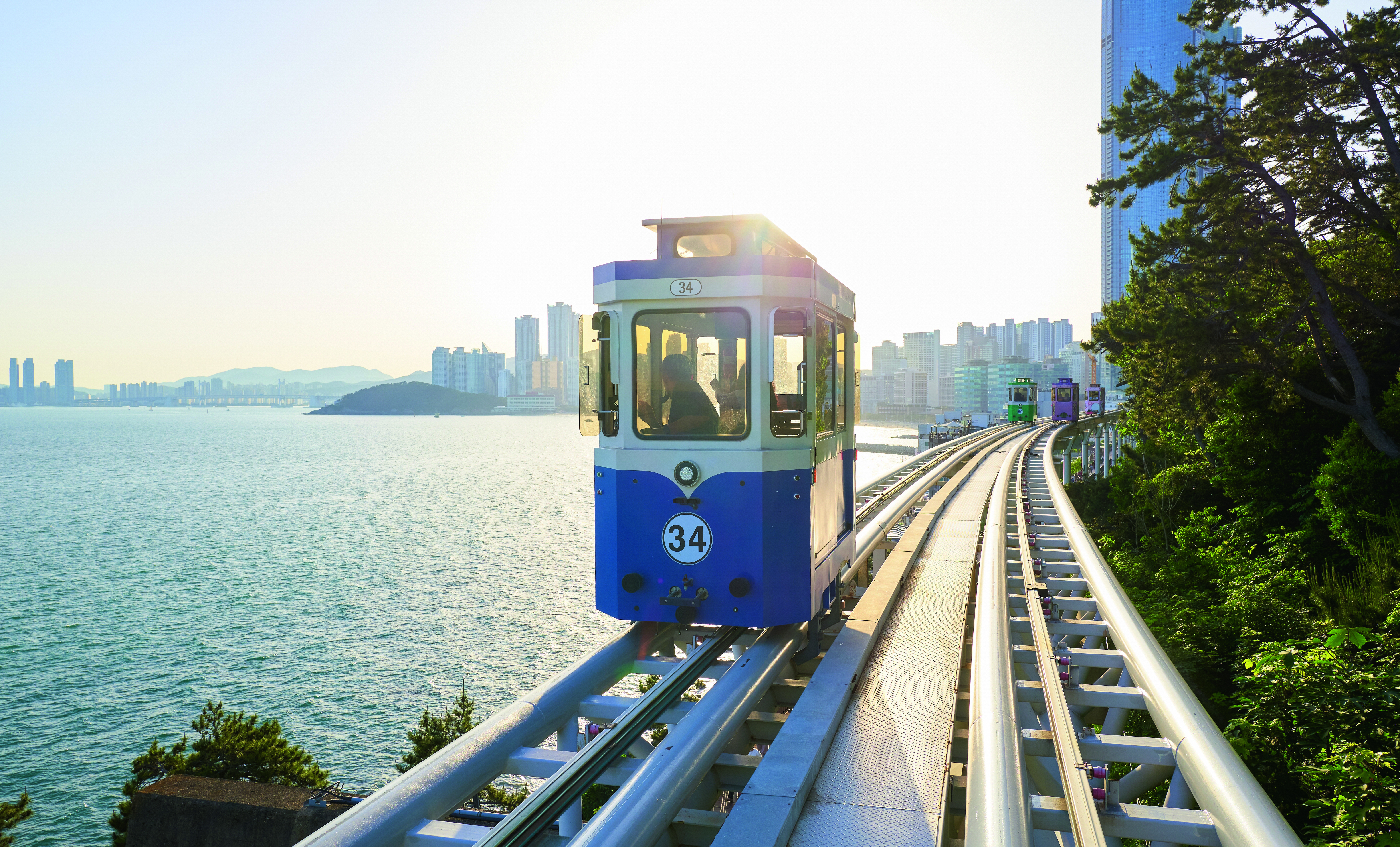 Eine Seilbahn mit der Nummer 34 fährt entlang einer Schiene mit Blick auf das Wasser und die Stadtlandschaft.