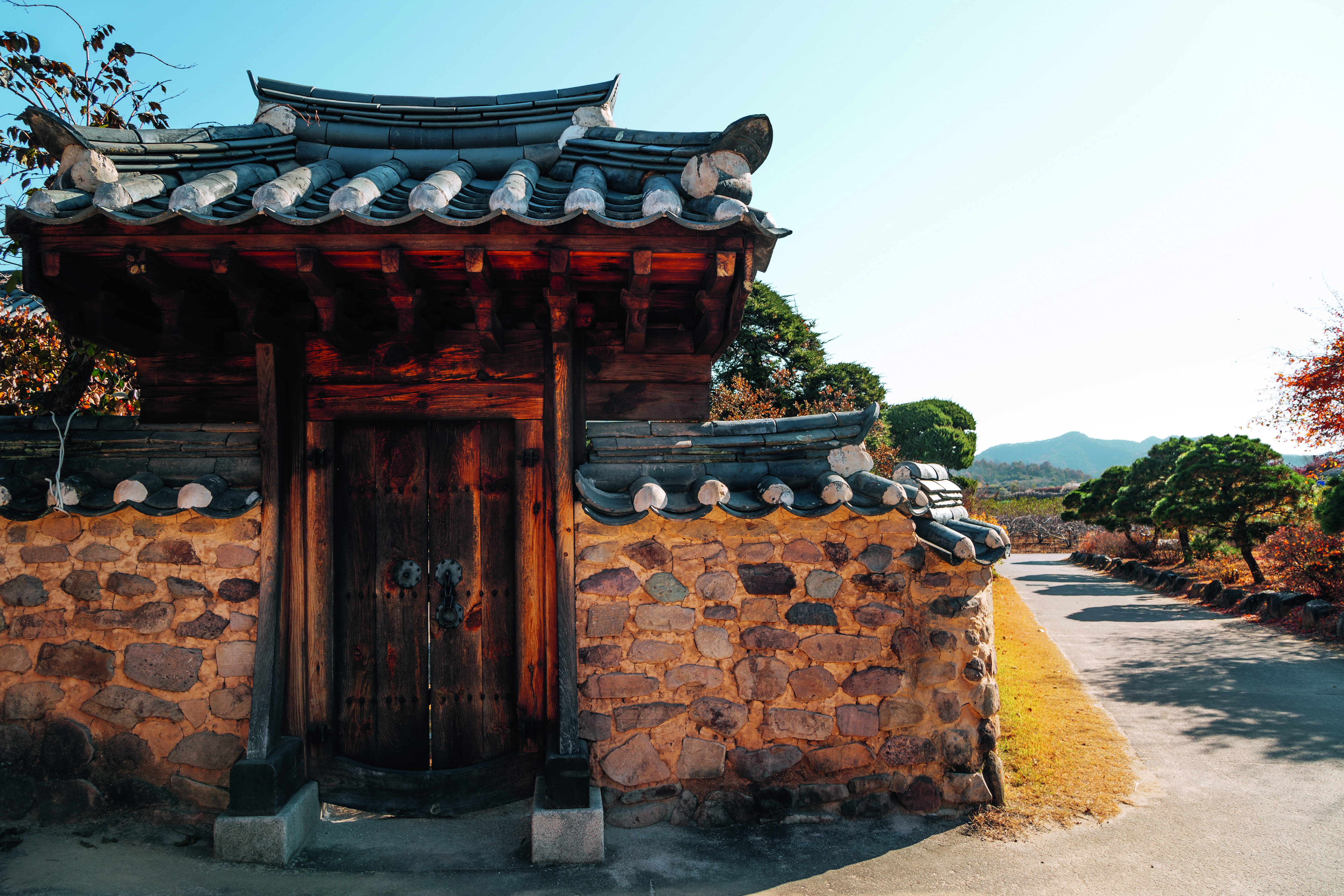 Traditionelles koreanisches Tor aus Holz und Stein mit einem gewölbten Dach in einem ländlichen Bereich.