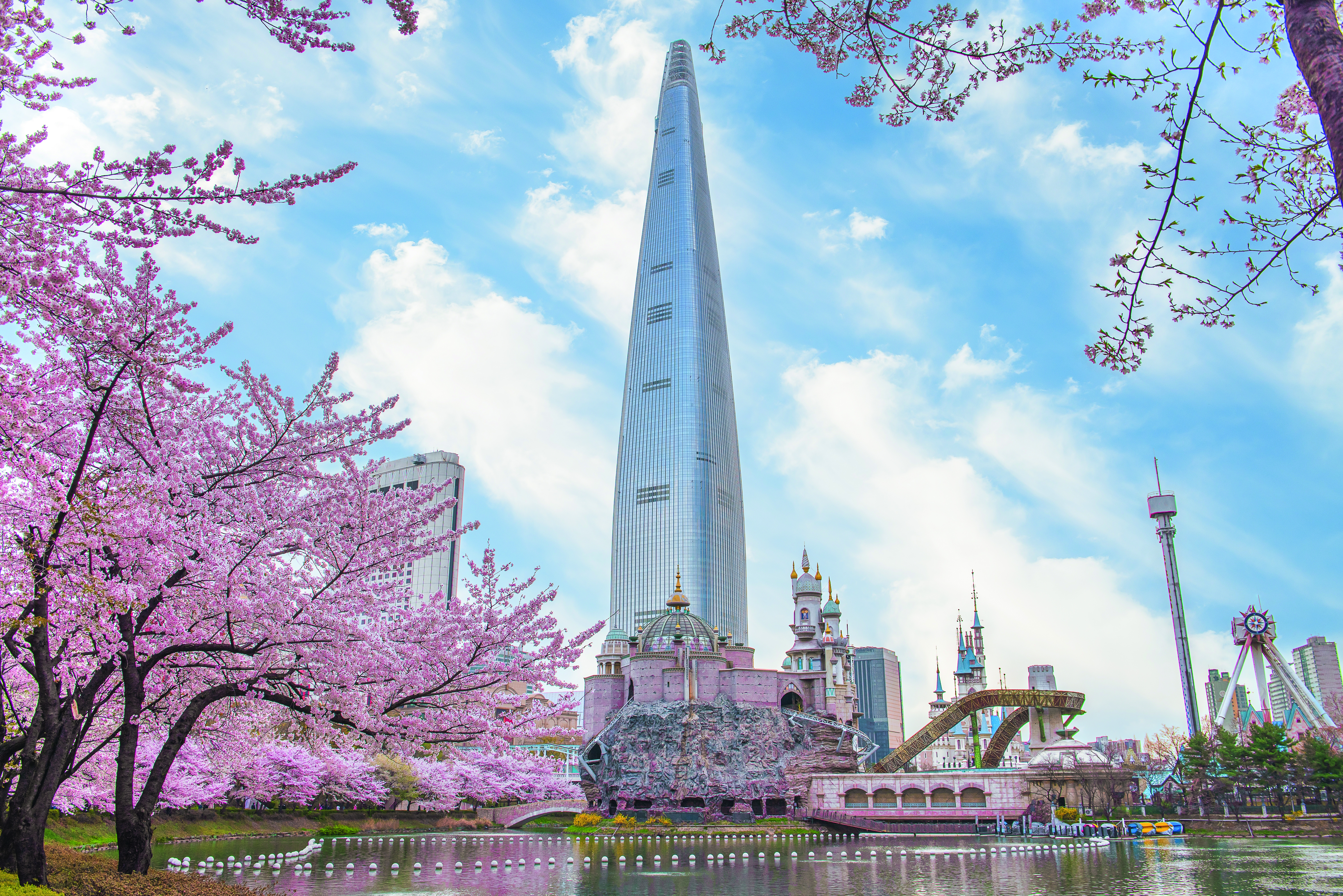Lotte World Tower in Seoul, umgeben von blühenden Kirschbäumen und einem klaren blauen Himmel.