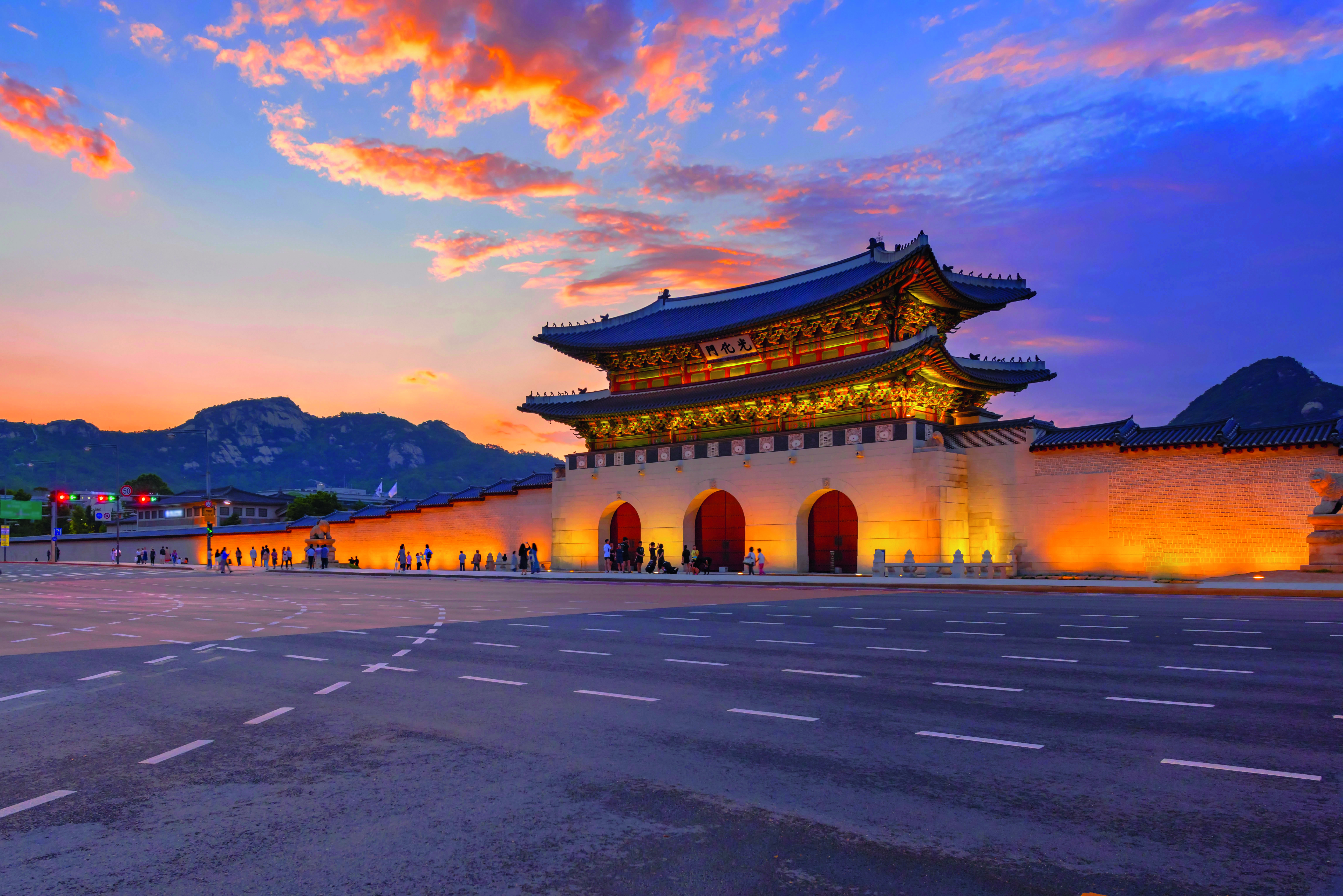 Gwanghwamun-Tor in Seoul bei Sonnenuntergang mit orangefarbenem Himmel und beleuchtetem Tor.