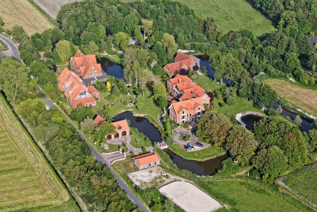 Luftaufnahme eines Wohngebiets mit roten Dächern, umgeben von Bäumen und Wasserflächen.