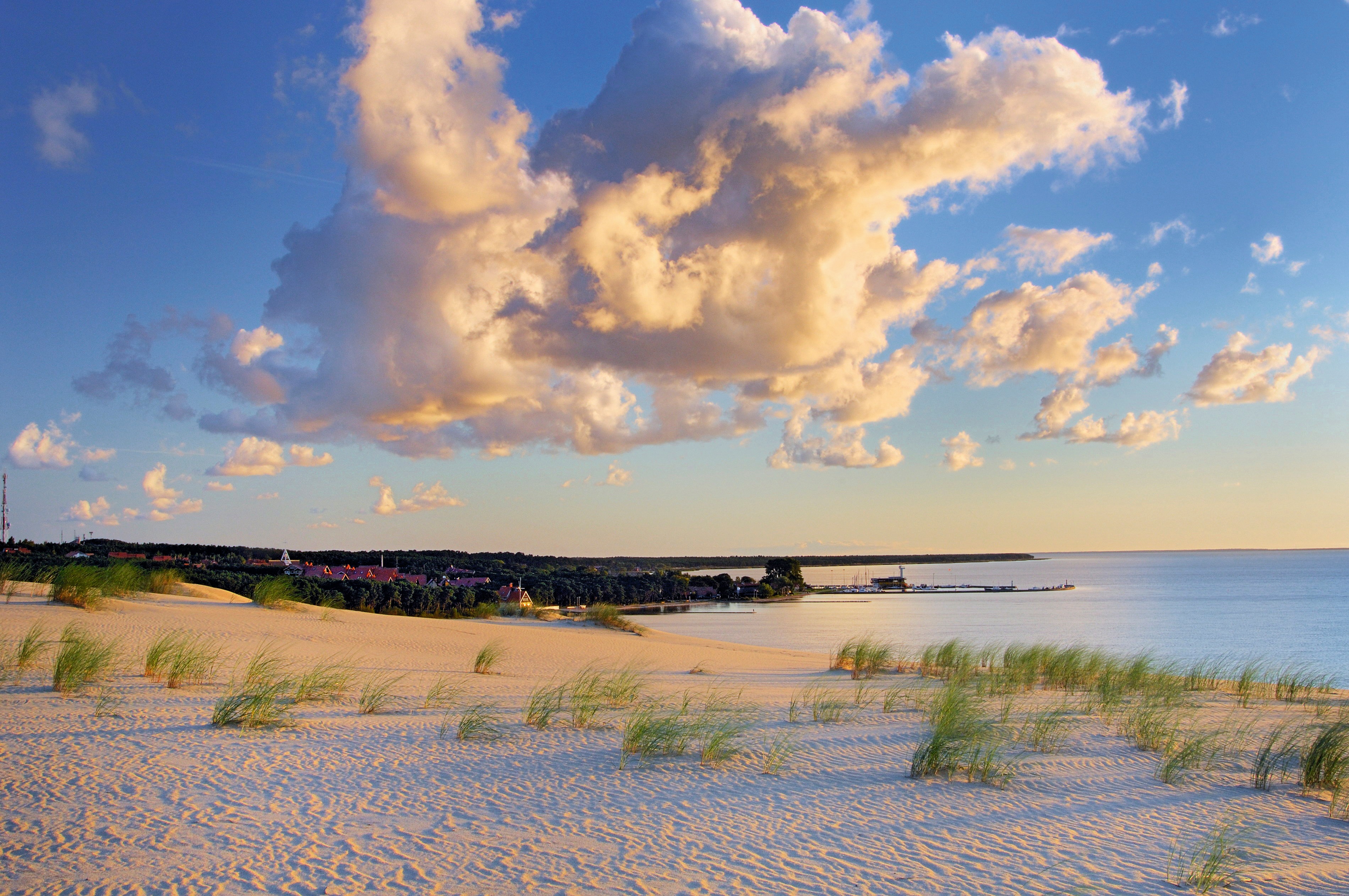 Sanddünen mit Gras und Wolken über der Kurischen Nehrung bei Sonnenuntergang.