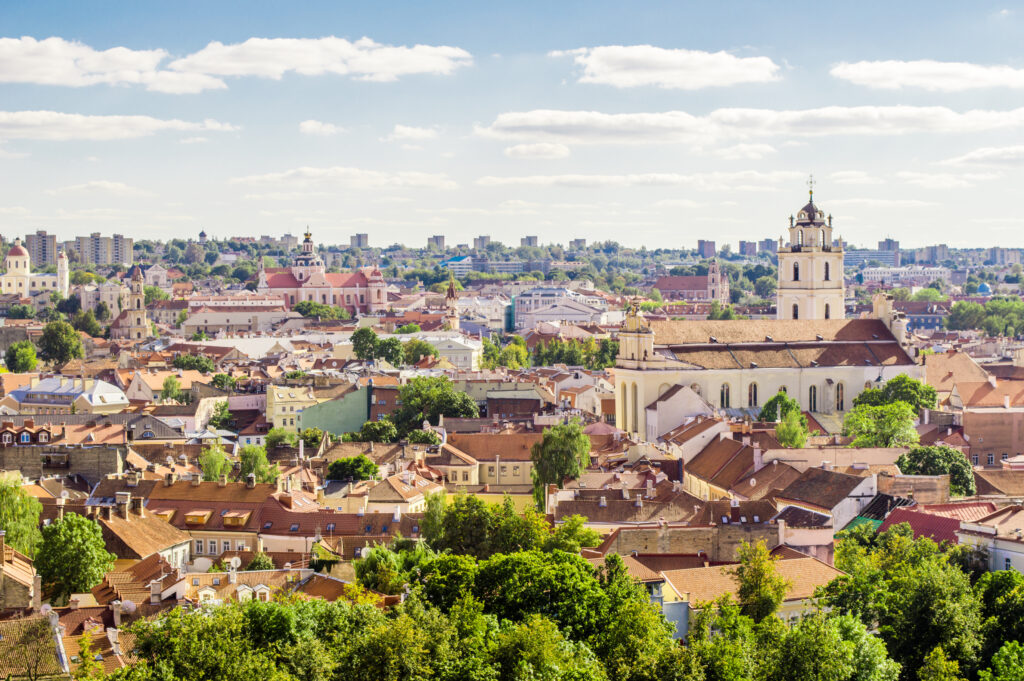 Blick auf die Altstadt von Vilnius mit historischen Gebäuden und grünen Bäumen unter blauem Himmel.