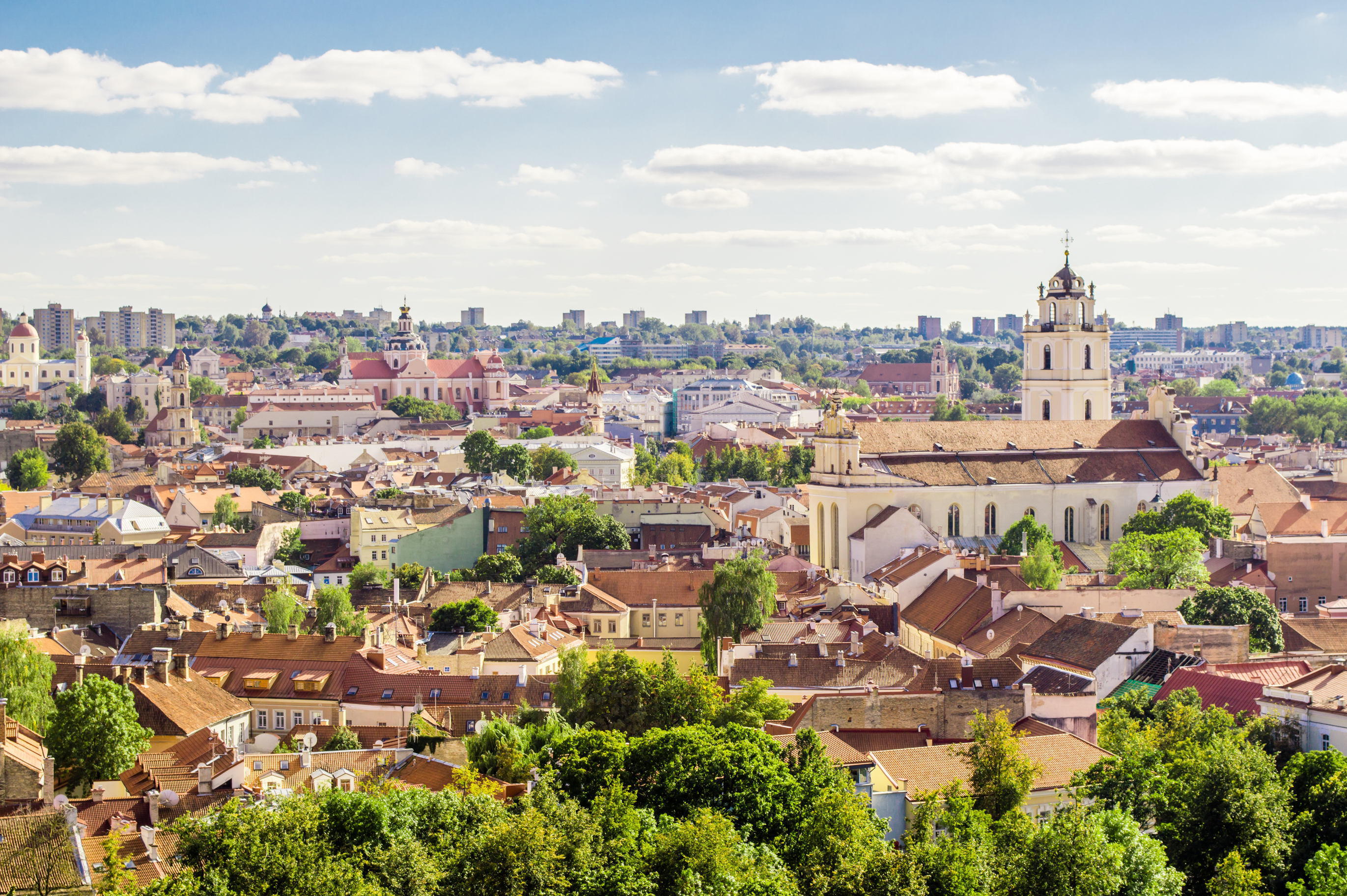 Blick auf die Altstadt von Vilnius mit historischen Gebäuden und grünen Bäumen unter blauem Himmel.