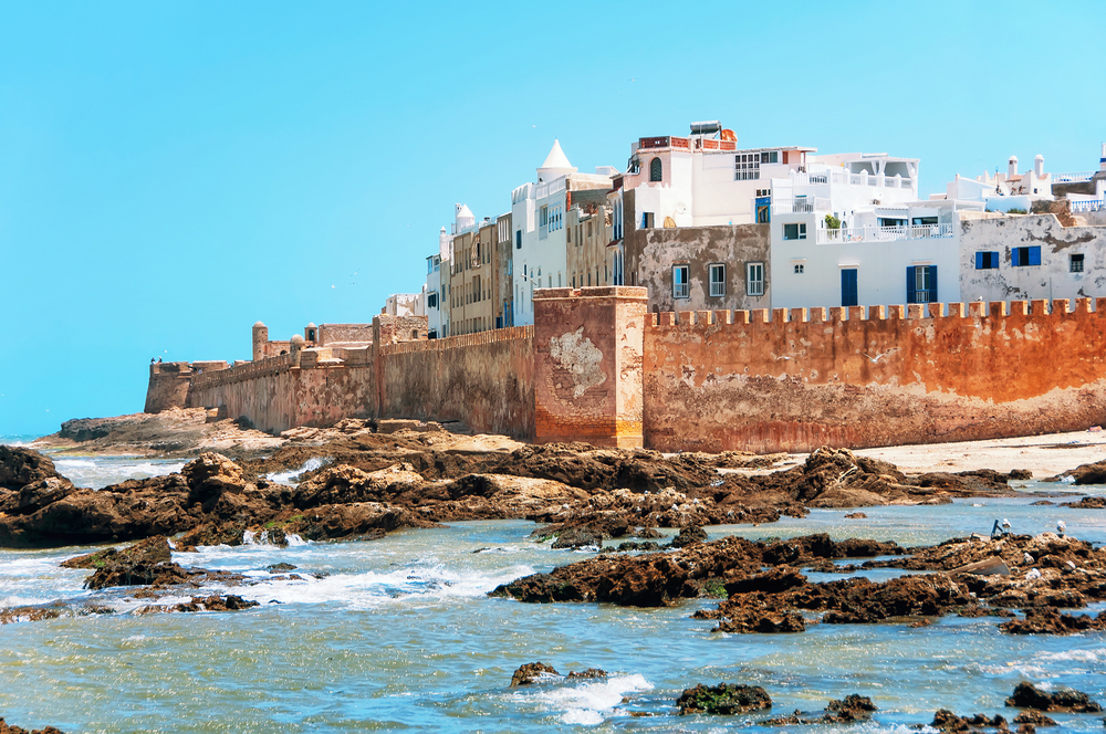 Blick auf die Stadt Essaouira mit der Stadtmauer und weißen Gebäuden am Meer.