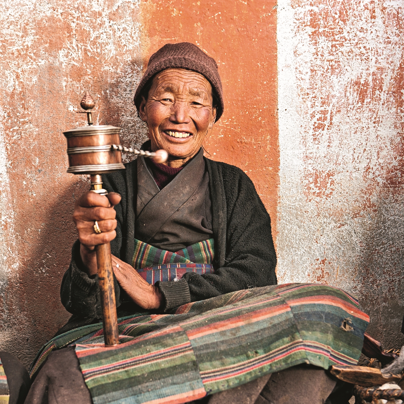 Eine ältere Frau hält eine Gebetsmühle in der Hand und lächelt freundlich. Sie trägt traditionelle Kleidung.