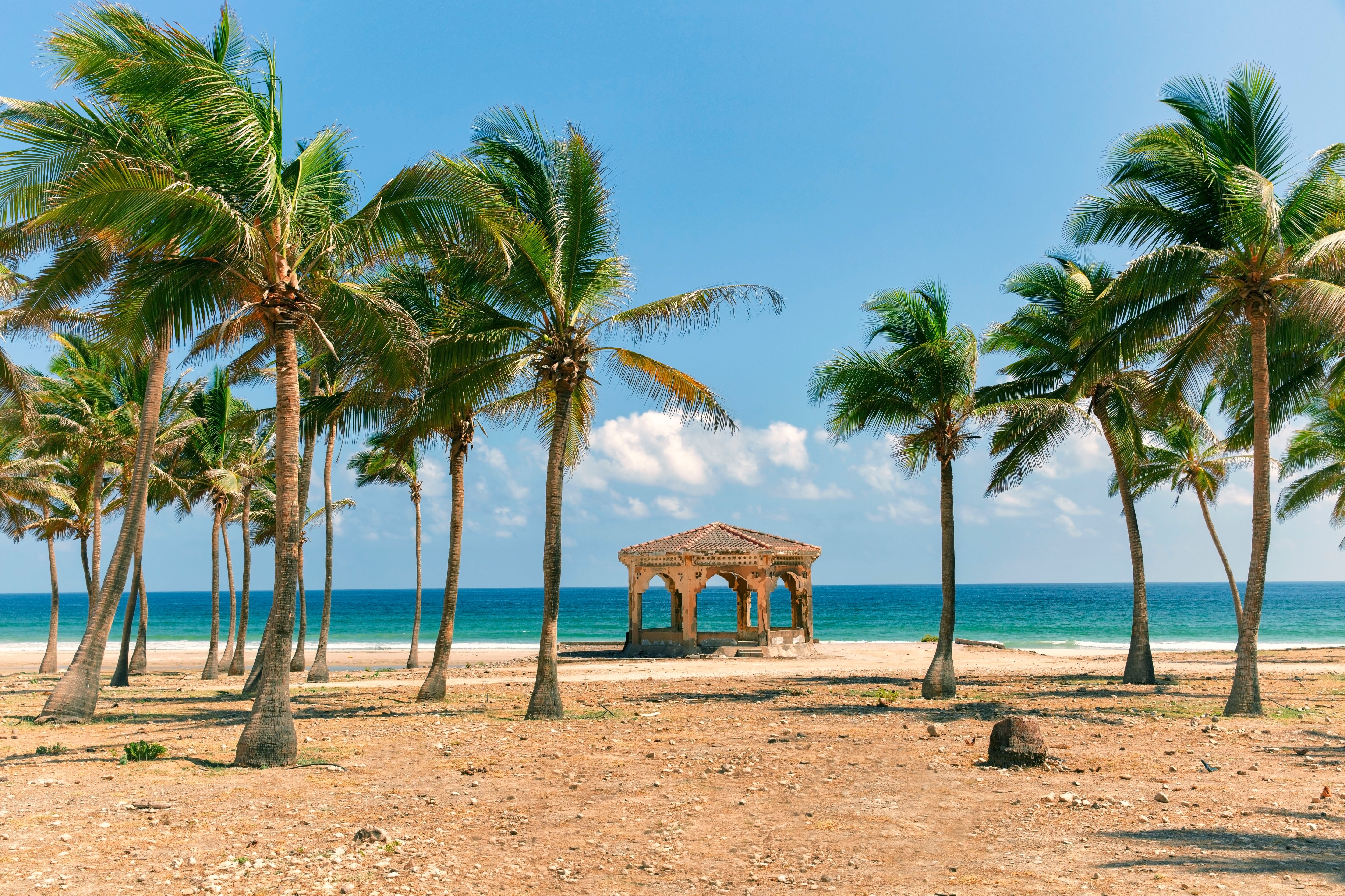 Ein Pavillon umgeben von Palmen am Strand mit Blick auf das Meer und den blauen Himmel.