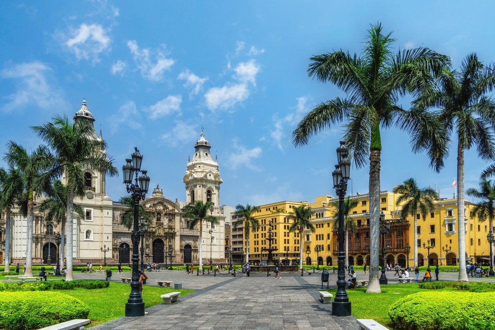 Plaza de Armas in Lima mit Palmen, historischen Gebäuden und blauem Himmel.