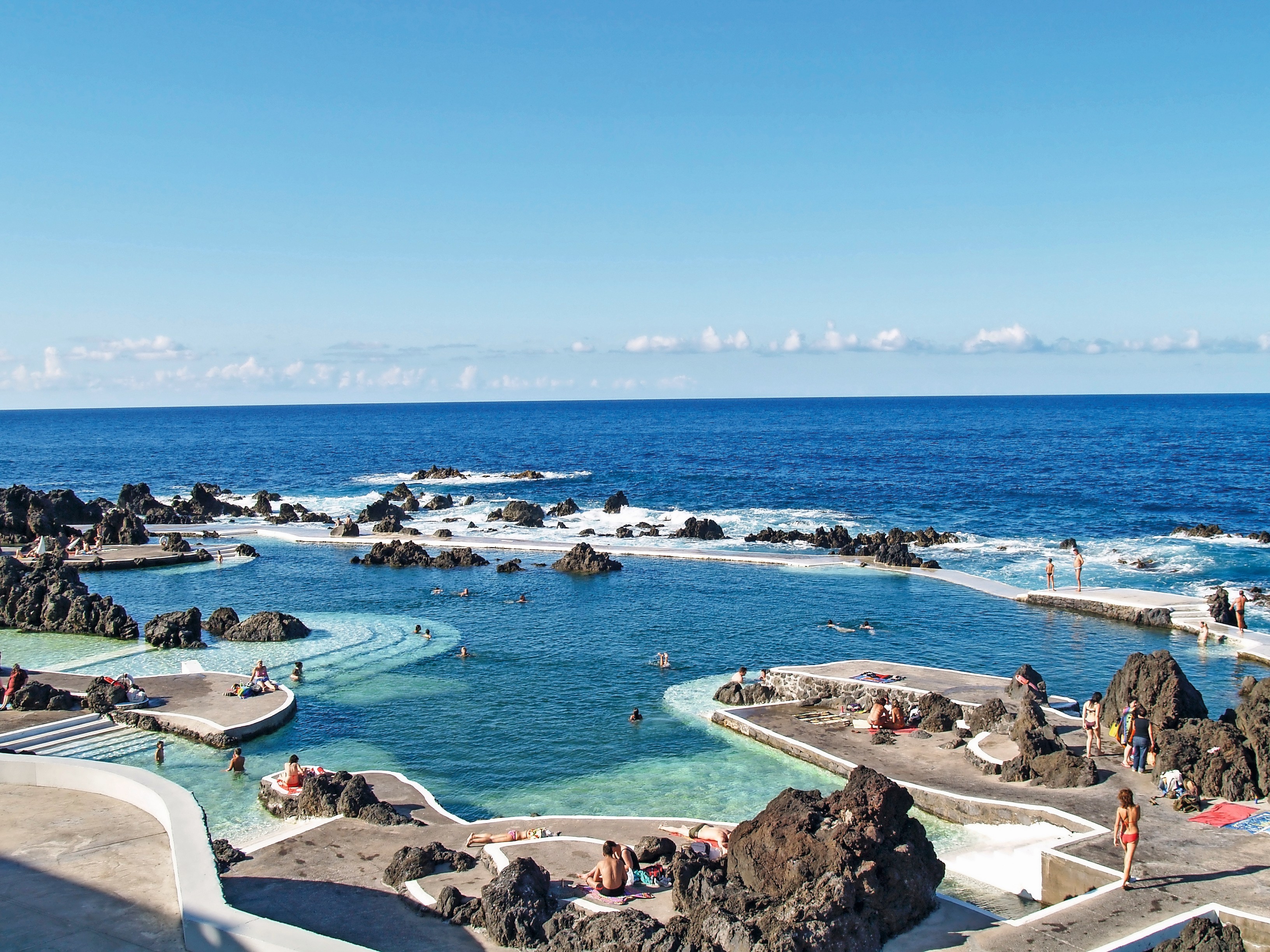 Natürliche Schwimmbecken aus Lavafelsen in Porto Moniz, Madeira, mit klarem Wasser und Menschen, die schwimmen.