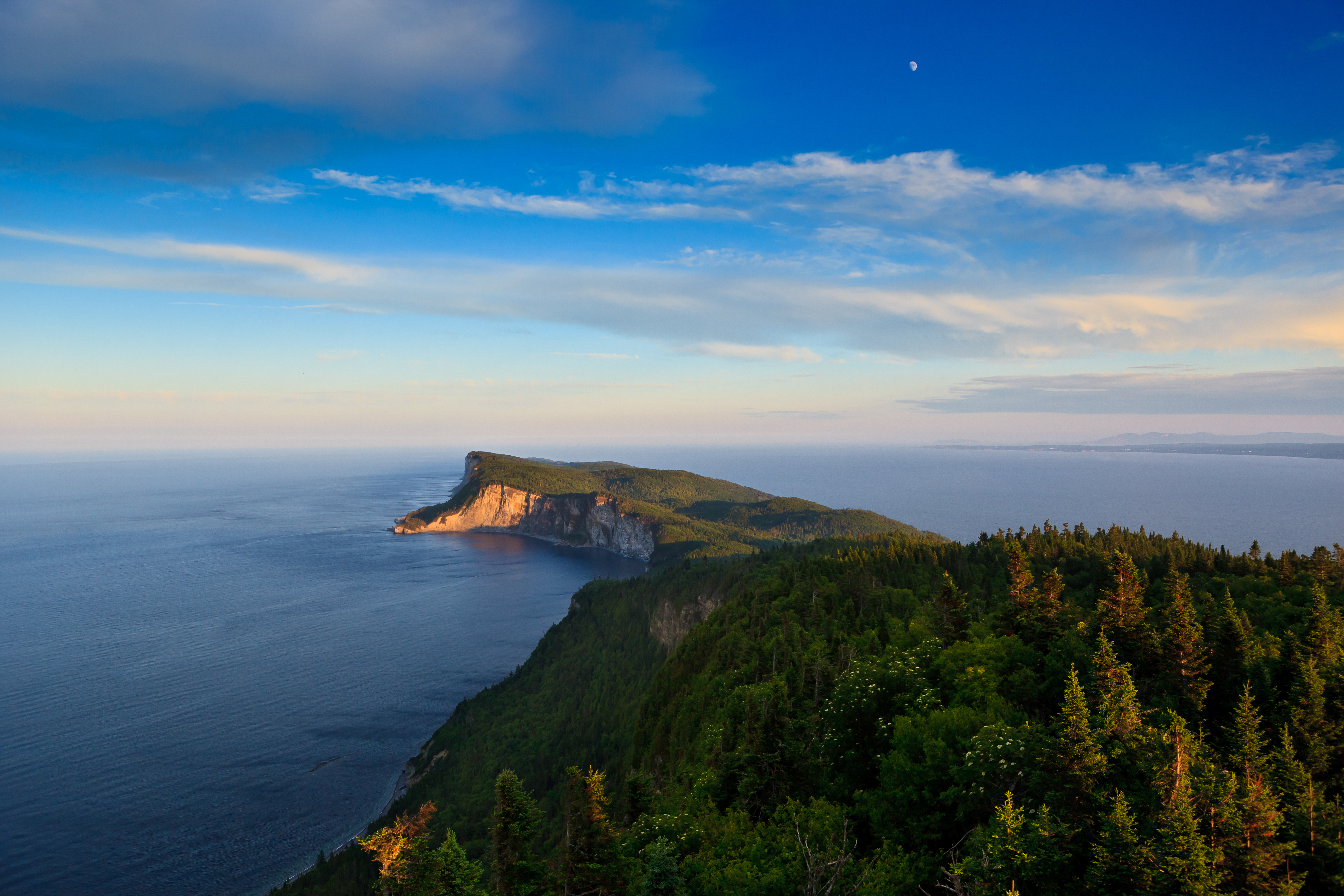 Blick auf eine Küstenlinie mit bewaldeten Hügeln und dem Meer im Hintergrund unter einem klaren Himmel.