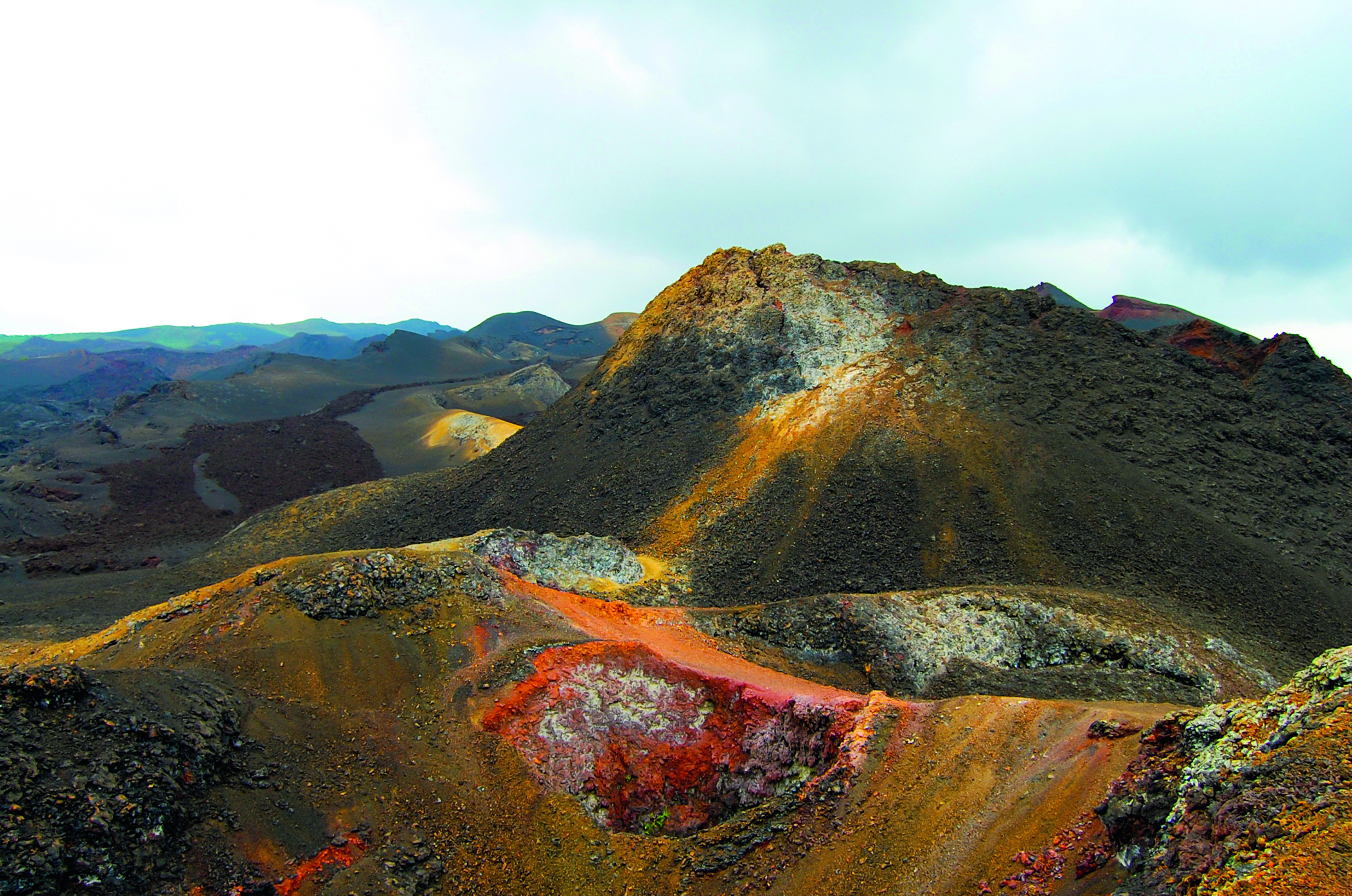 Landschaft mit vulkanischen Hügeln und bunten Erdmischungen in einem Gebirgszug.