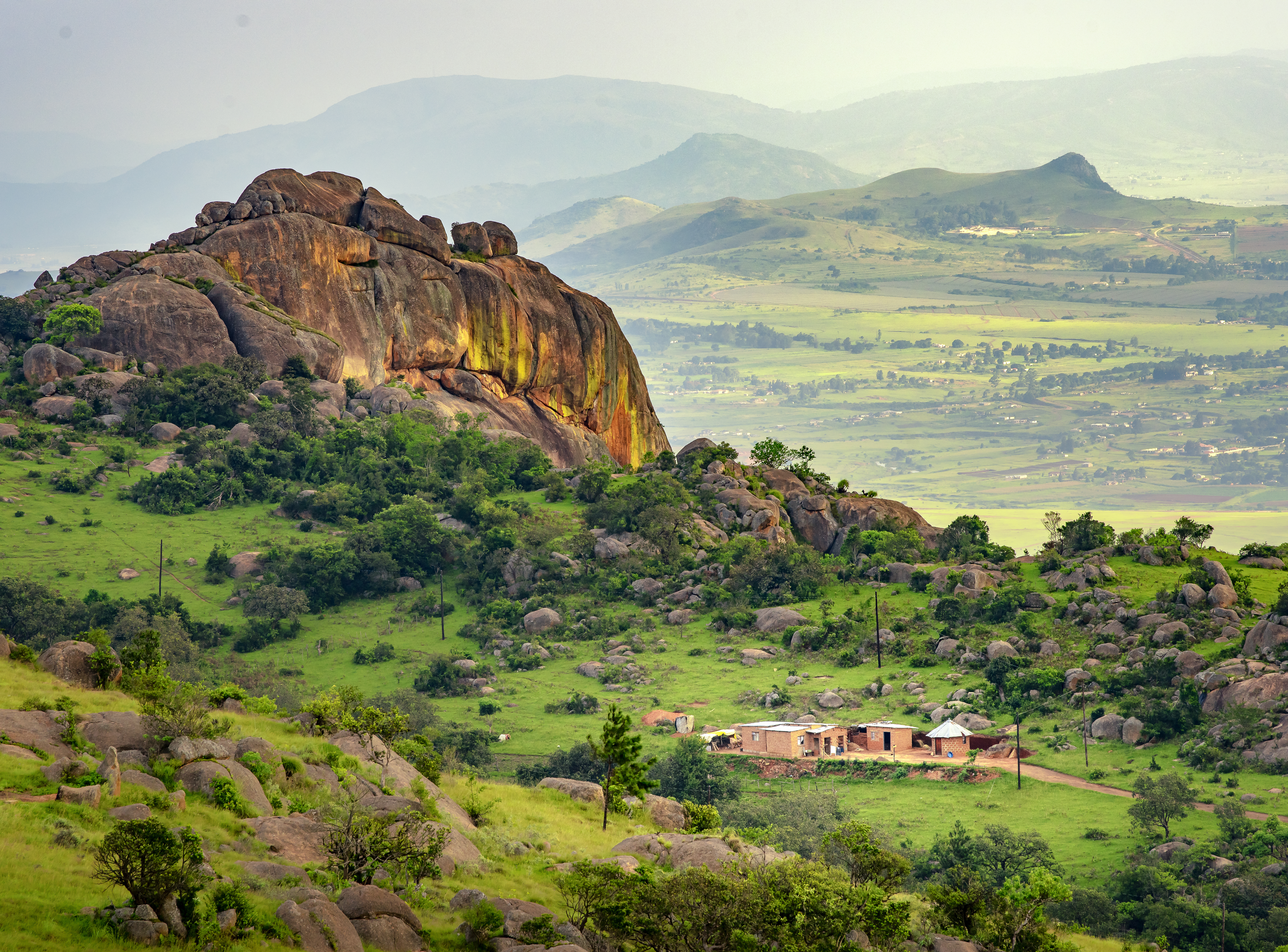 Eine grüne Landschaft mit einem großen Felsen und einem kleinen Gebäude im Vordergrund.
