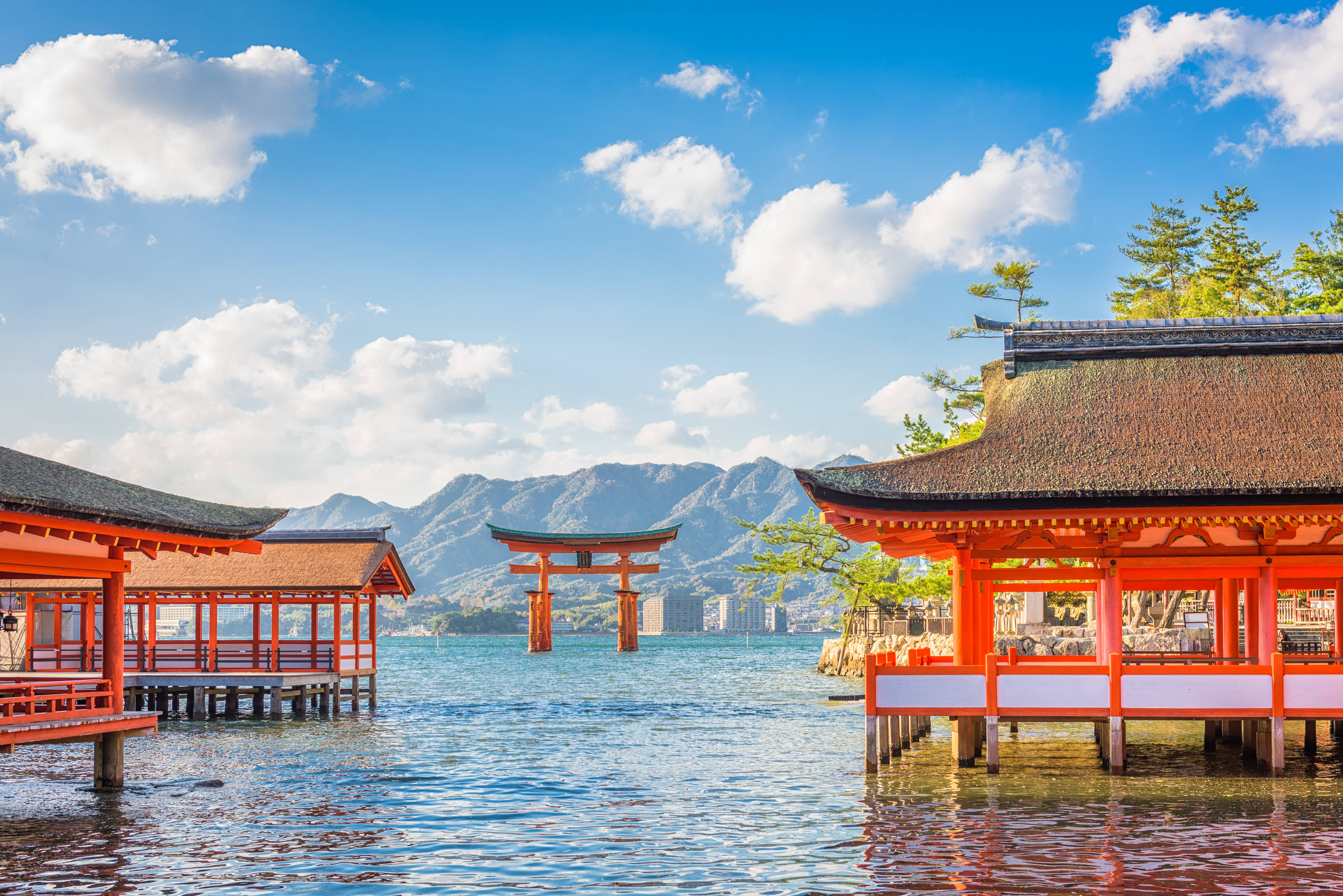 Rote Torii und traditionelle japanische Gebäude am Wasser mit Bergen im Hintergrund.