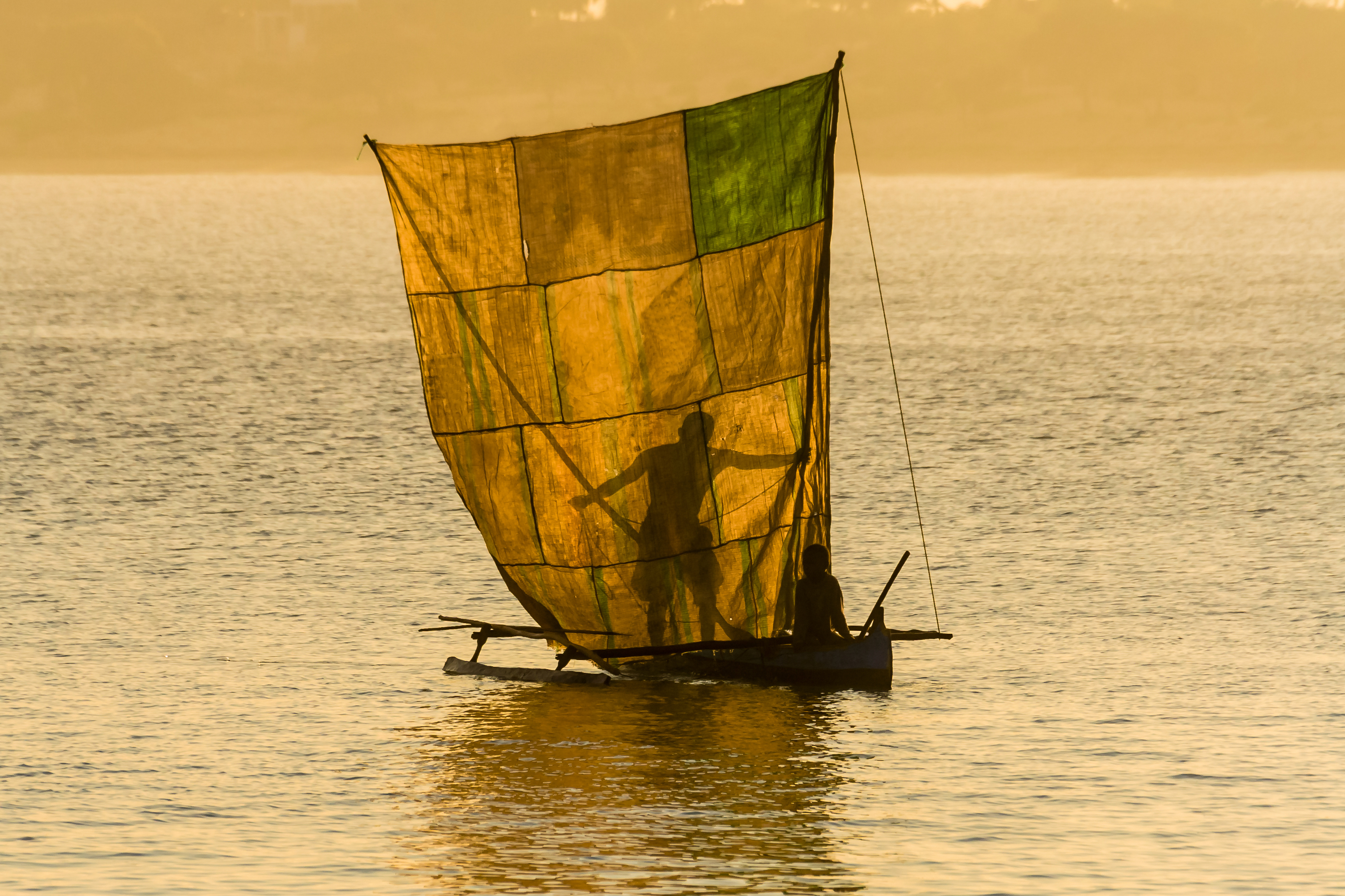 Fischerboot mit gelbem und grünem Netz auf ruhigem Wasser bei Sonnenuntergang.