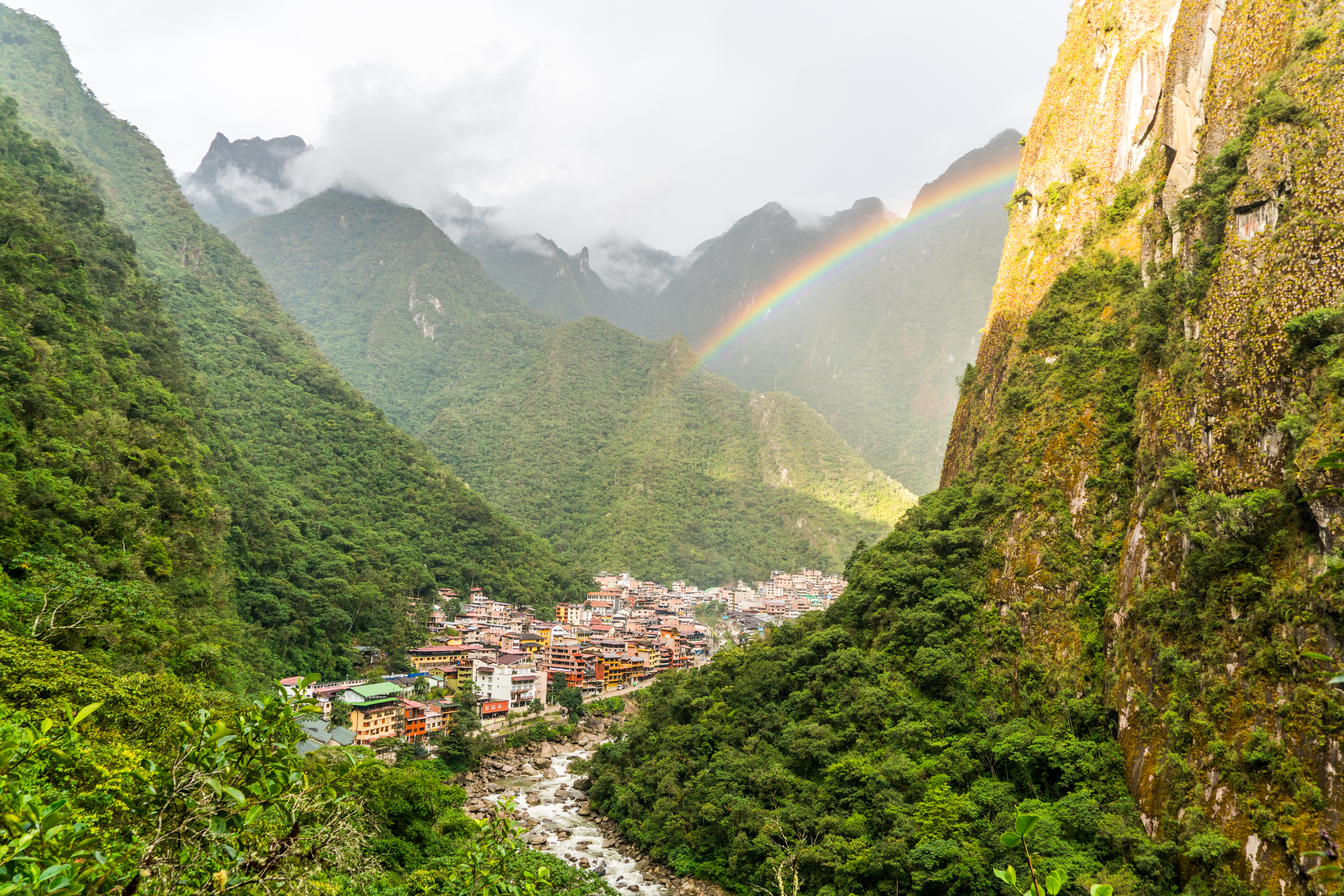 Blick auf Machu Picchu mit Regenbogen über den Bergen und der Stadt im Tal.