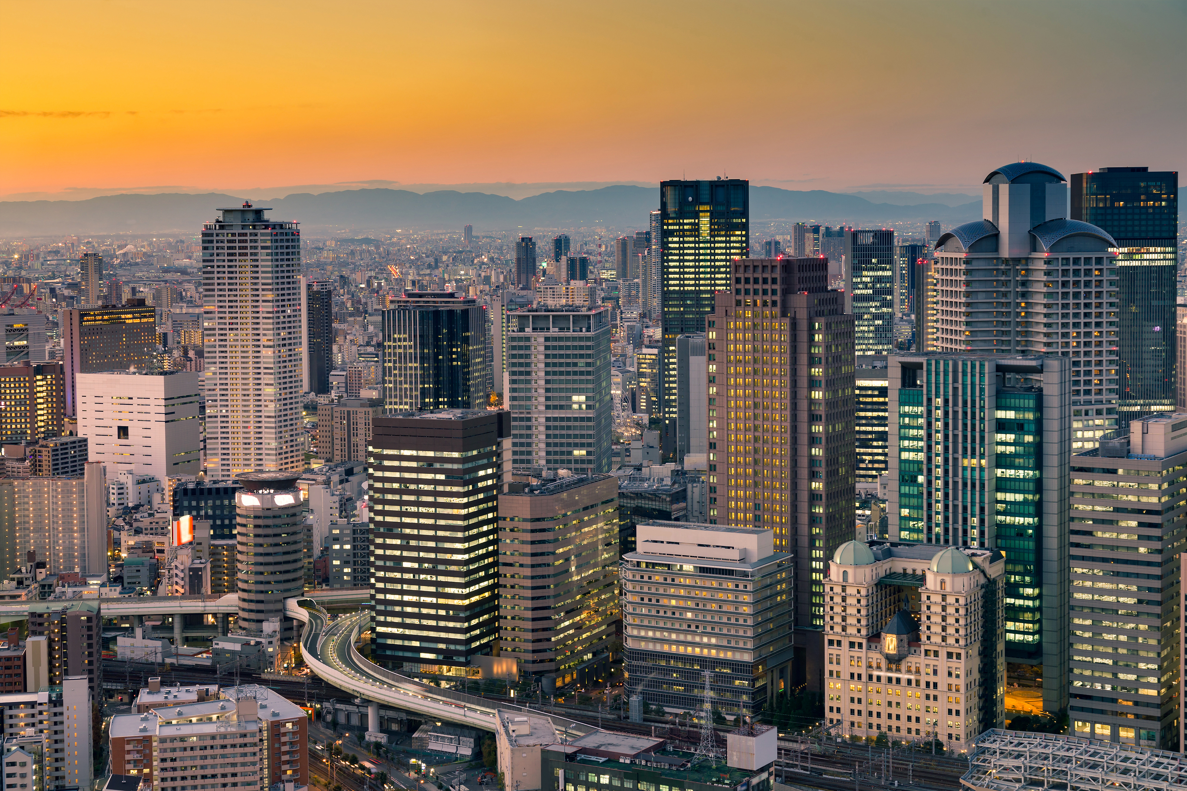Stadtansicht von Osaka mit modernen Wolkenkratzern und einer untergehenden Sonne im Hintergrund.