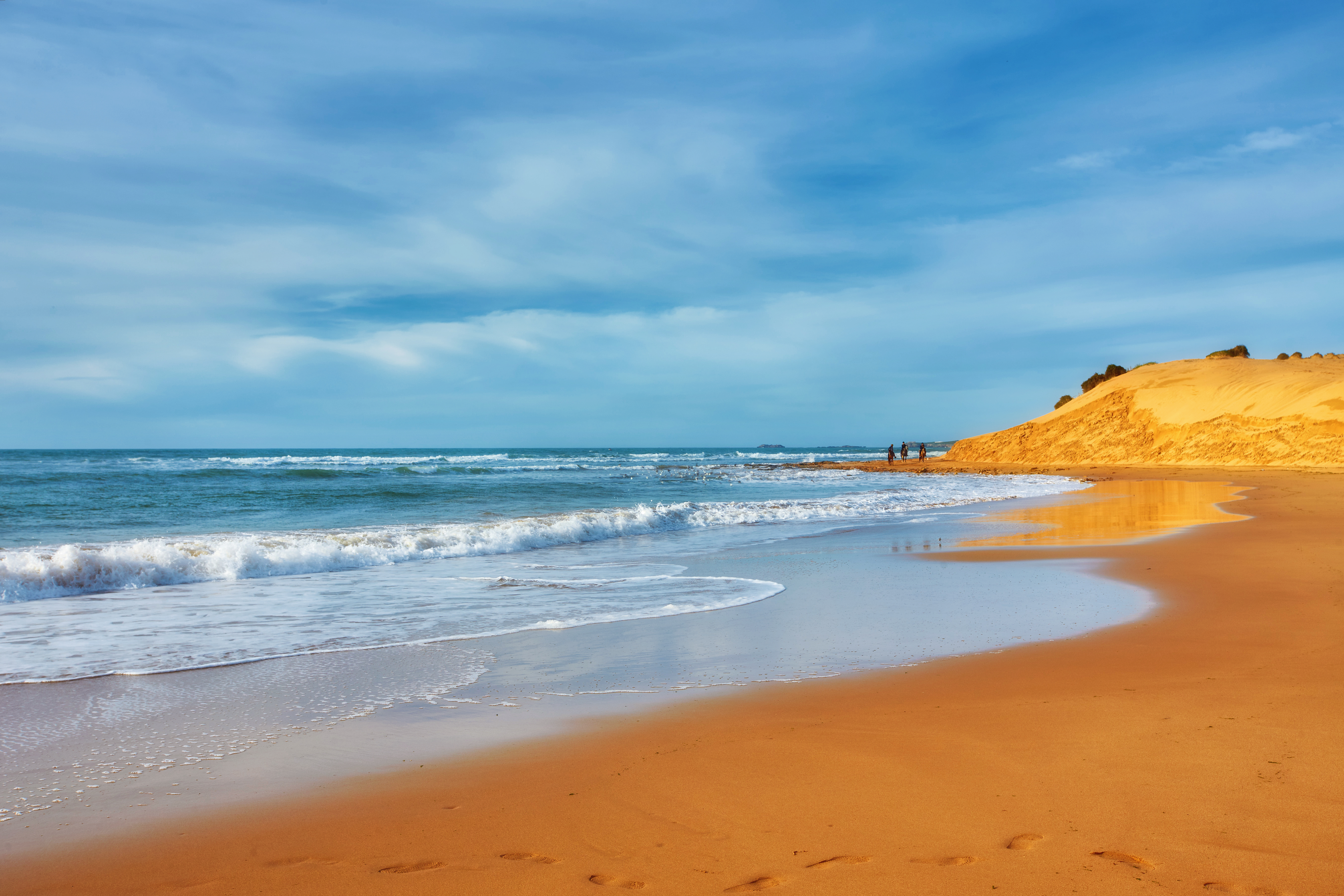 Strand mit sanften Wellen und goldfarbenem Sand unter einem klaren Himmel.