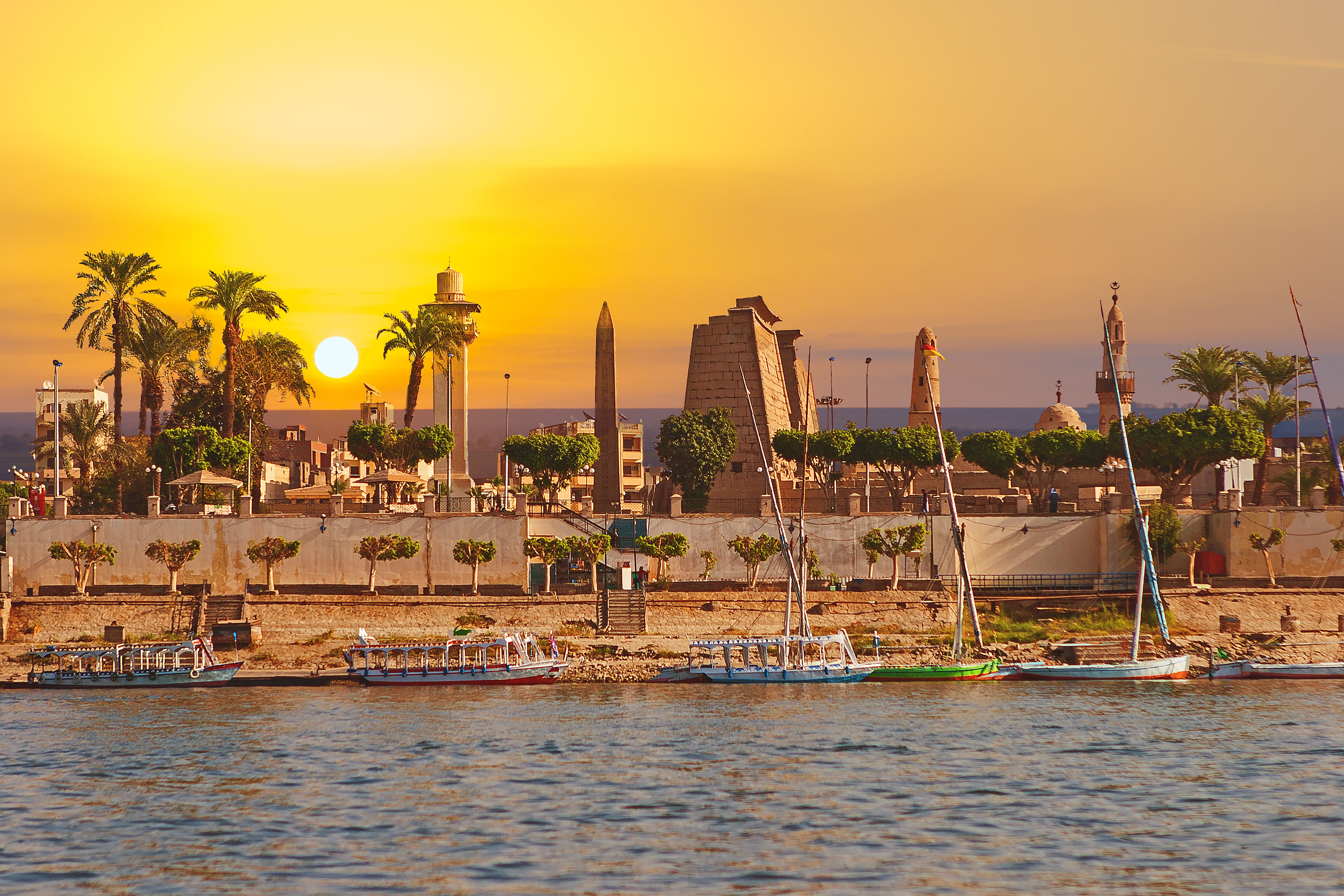 Sonnenuntergang über dem Nil mit traditionellen Feluken und historischen Monumenten in Luxor, Ägypten.
